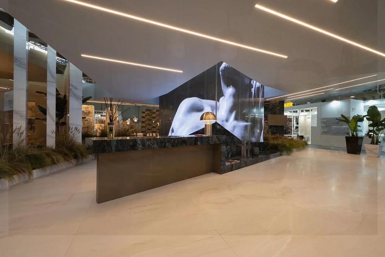 Area di ricevimento moderna con bancone in marmo, schermi digitali che mostrano immagini in bianco e nero, illuminazione a LED e decorazioni verdi. arch-12 A-12  Simone Rosi design