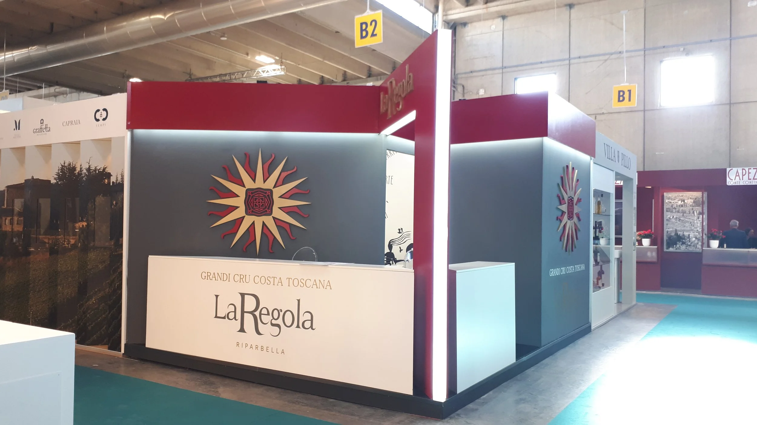 Stand promozionale di La Regola a una fiera, con decorazioni a tema vinicolo e cartelli indicanti lo spazio espositivo nelle sezioni B1 e B2.