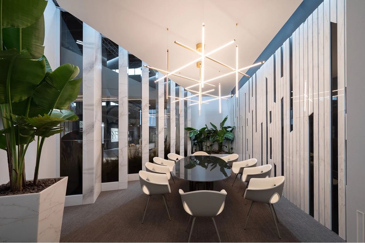 Sala riunioni moderna con un grande tavolo ovale nero, sedie bianche, piante decorative e illuminazione pendente contemporanea. Pannelli di marmo e vetro decorano le pareti.arch-12 A-12  Simone Rosi design