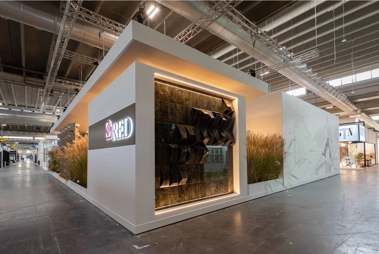 Stand fieristico moderno con piante ornamentali e logo "RED" su un muro decorativo nero. arch-12 A-12  Simone Rosi design