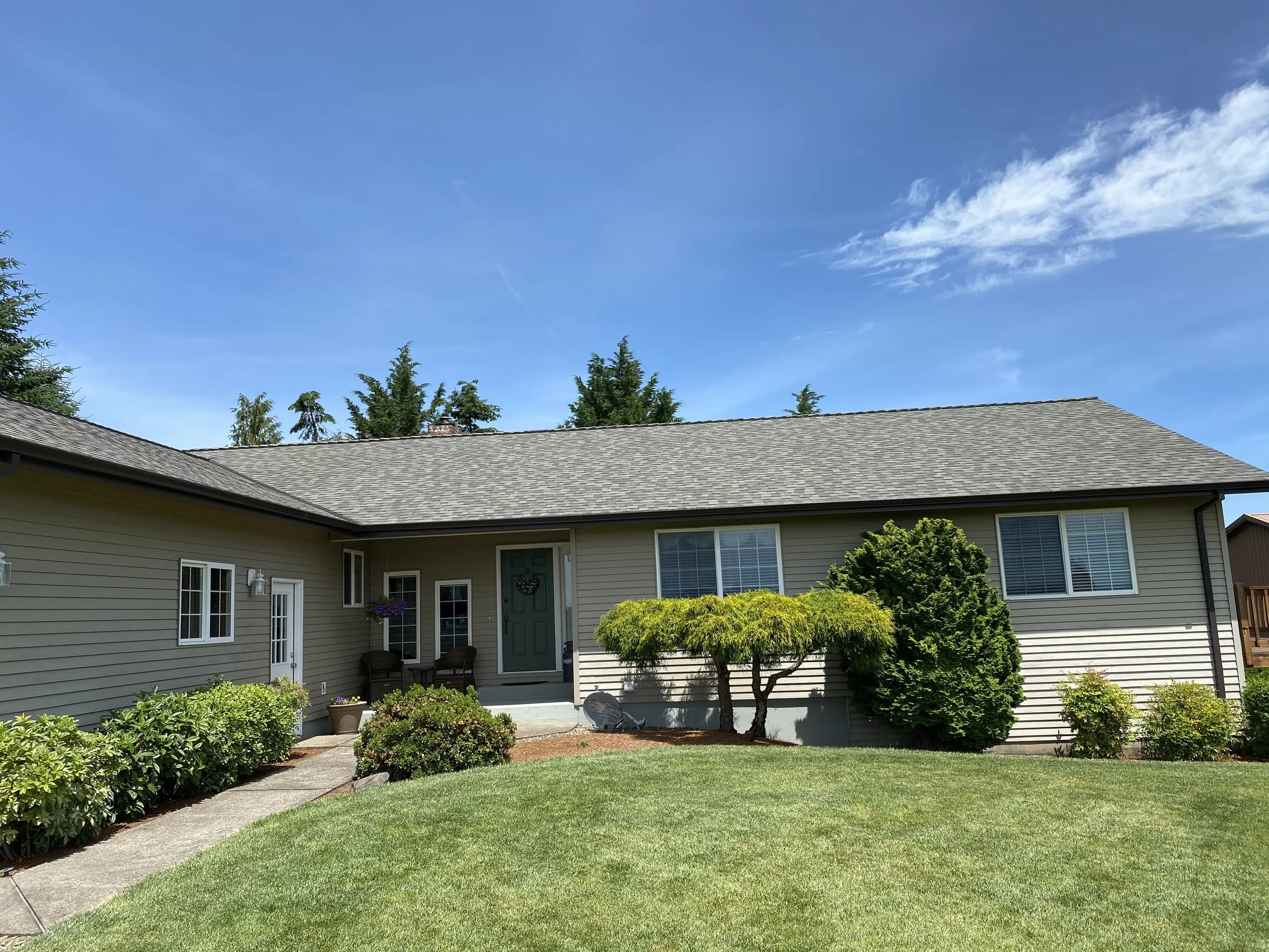 One-story suburban house with green lawn and shrubs, blue sky background.
