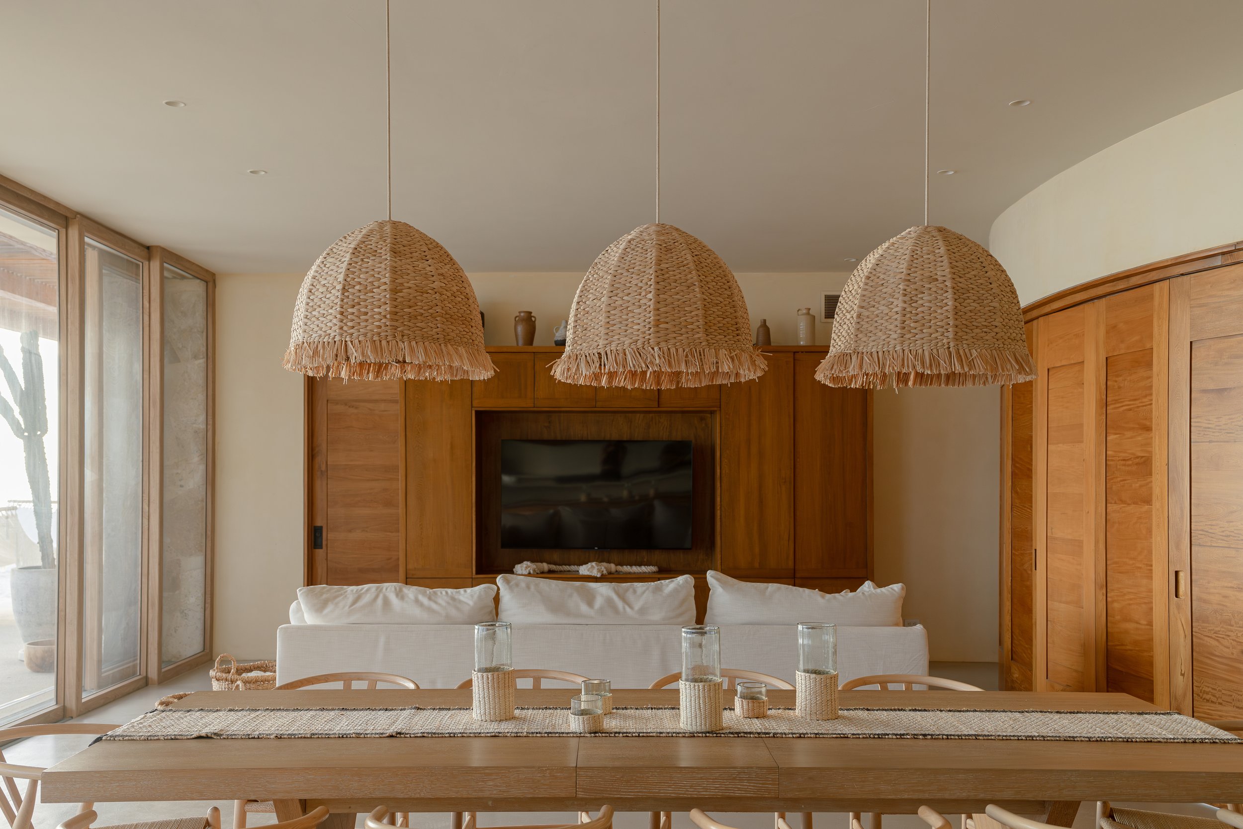 Modern living room with a wooden dining table, pendant lights, and a couch facing a TV on a wooden wall unit.