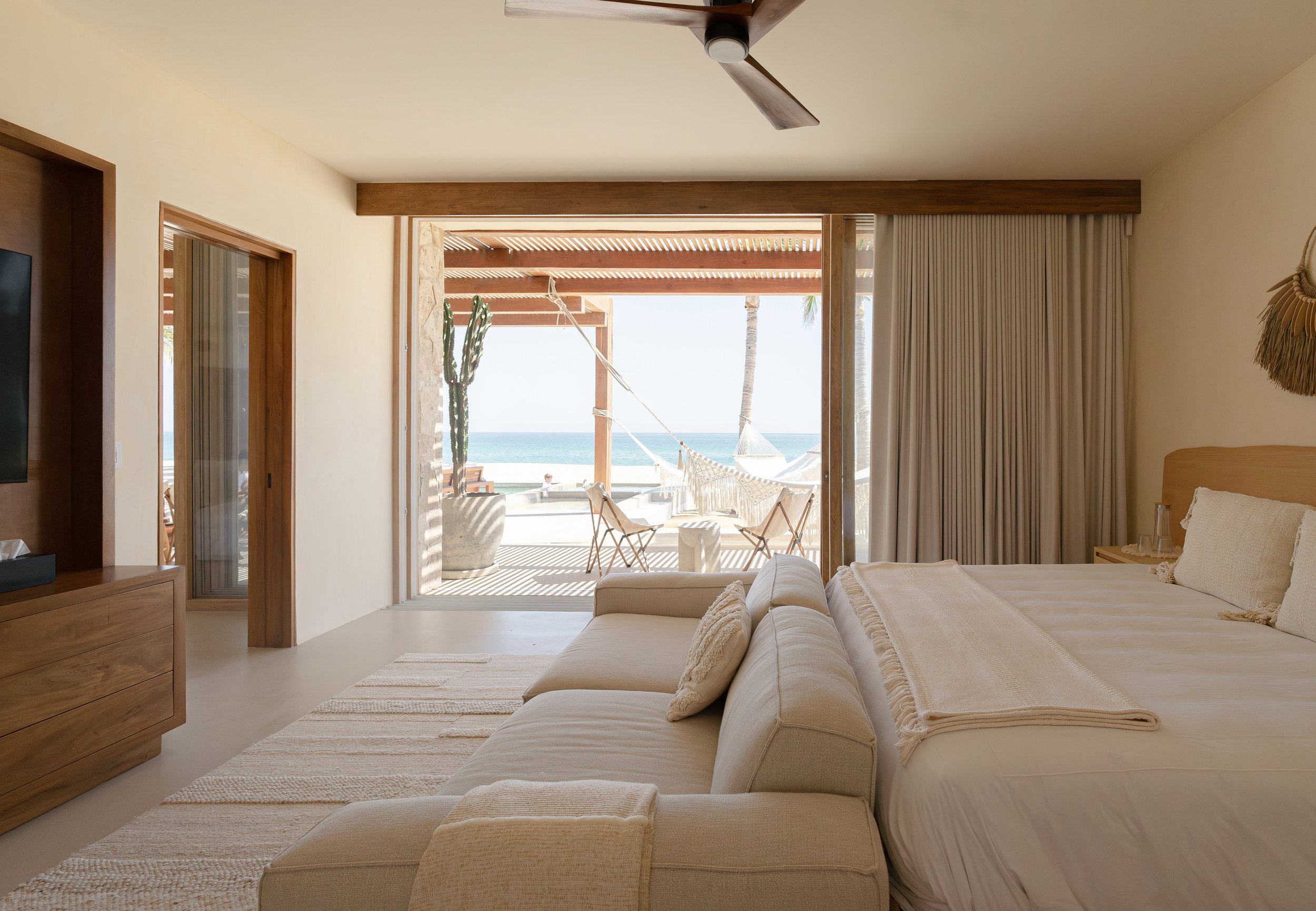 Luxurious beachfront hotel room with large bed, sofa, and sliding glass doors opening to a patio with a hammock and an ocean view.