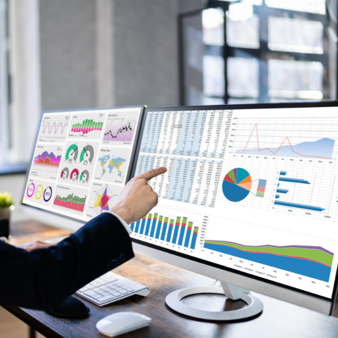 Person in a suit pointing at multiple monitors displaying data charts and graphs in a modern office.