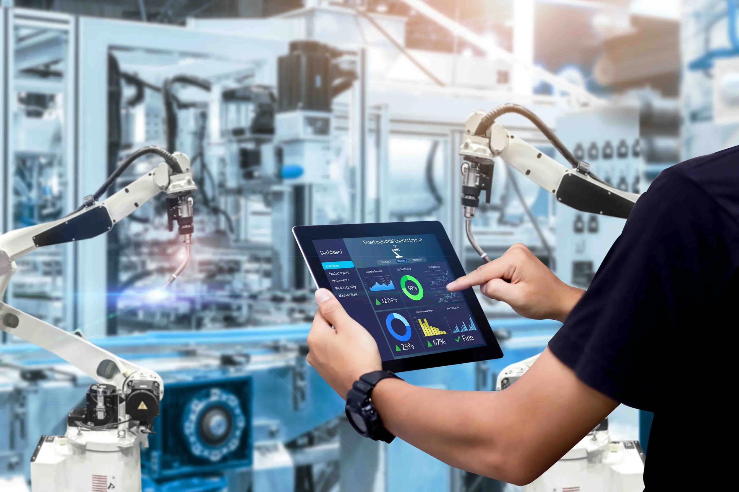 Person using a tablet with a smart industrial control system interface in a manufacturing or robotic automation setting with robotic arms and machinery in the background.