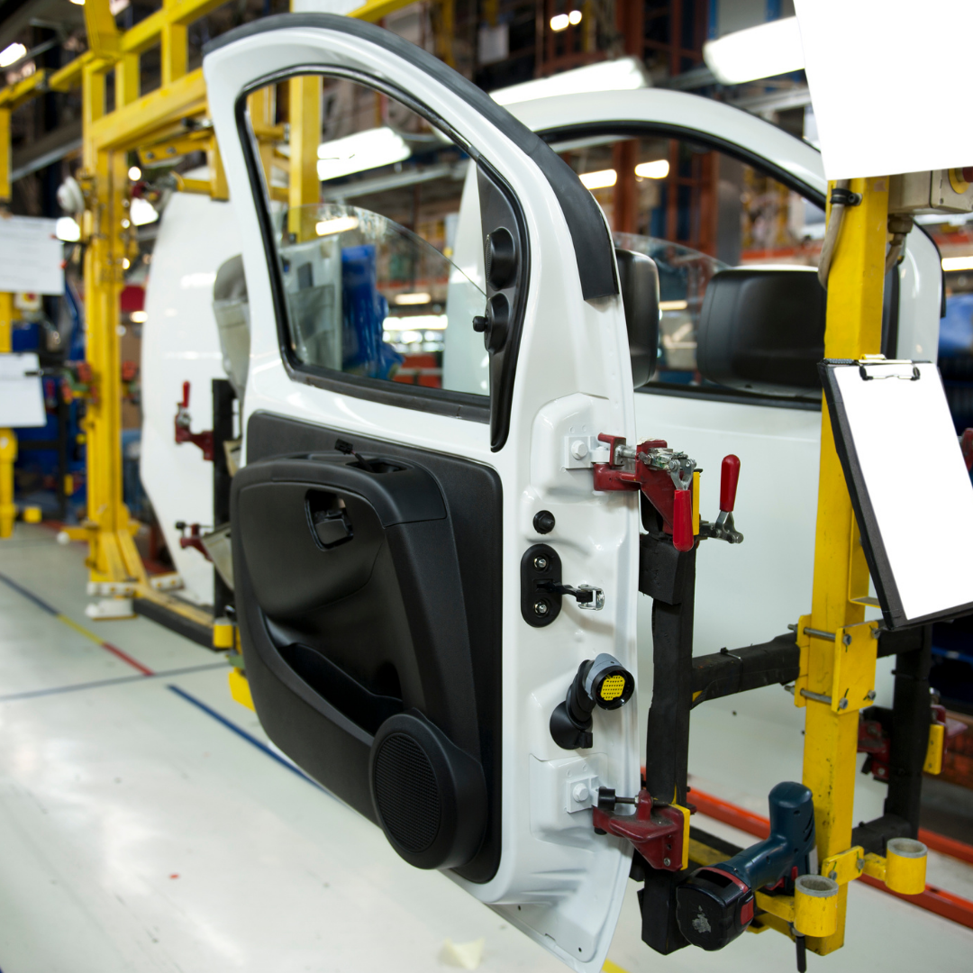 A car door assembly line in a manufacturing facility with yellow support structures and tools visible.