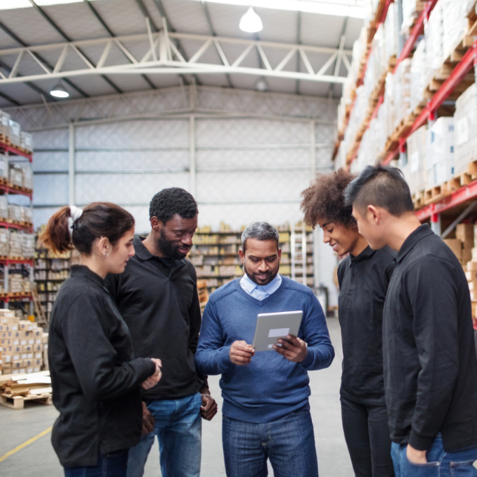 Group of five workers in a warehouse looking at a tablet.
