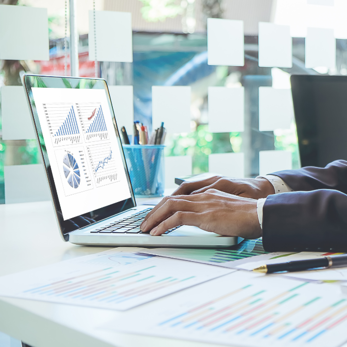 Person in business suit working on a laptop displaying financial graphs and charts in an office.