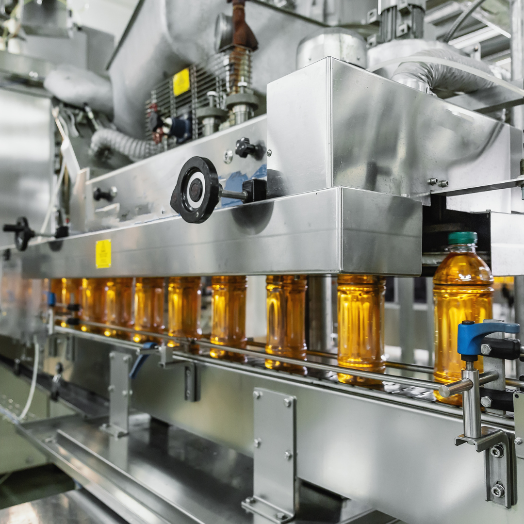 Automated bottling machine filling glass bottles with yellow liquid in factory setting.