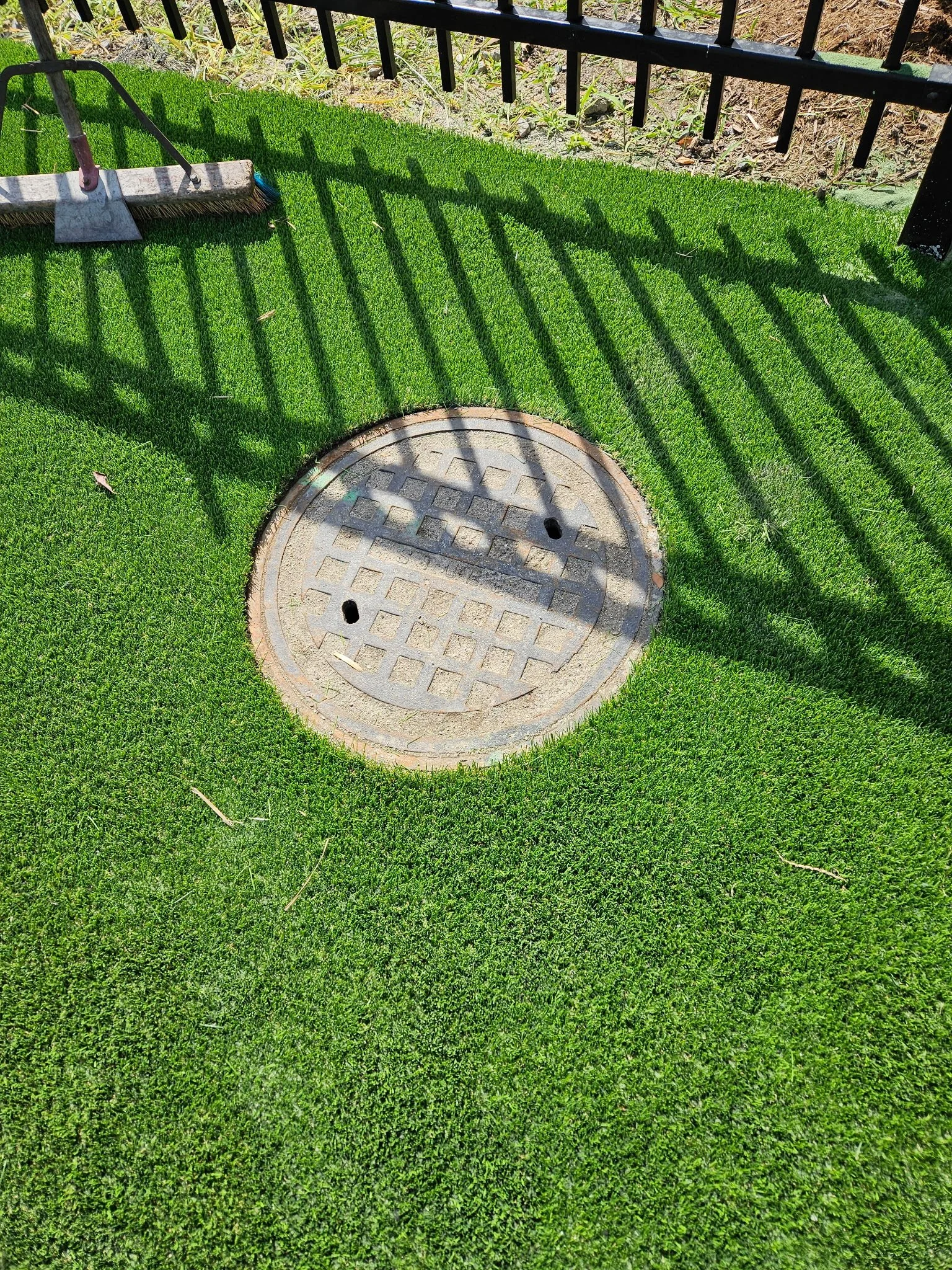 After — Precision cutting of artificial turf around a water/sewer cleanout cap for a clean, accessible finish.