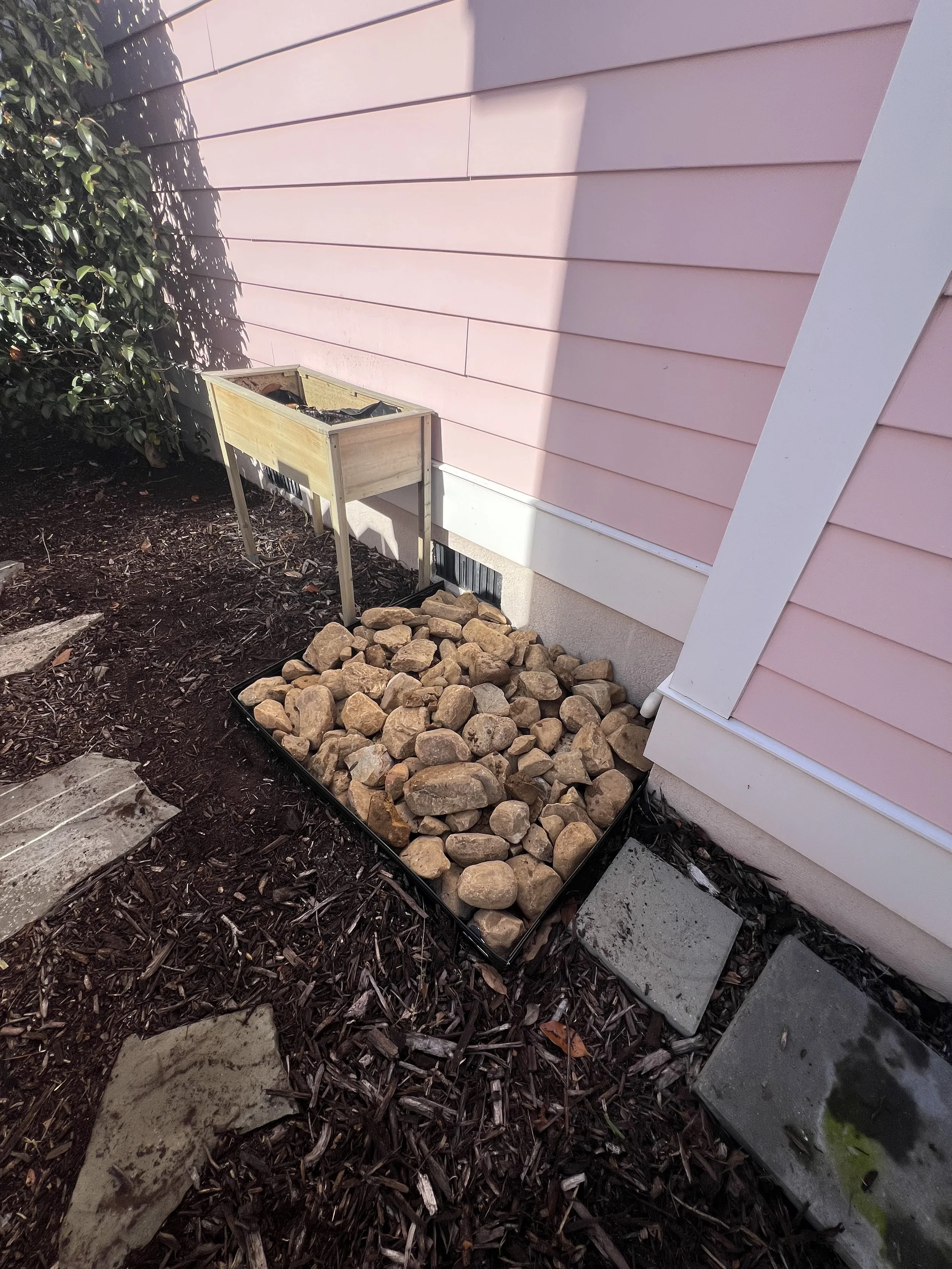 After — Splash zone installation for a no-gutter roof: graded runoff path with river rock pad to protect the foundation.