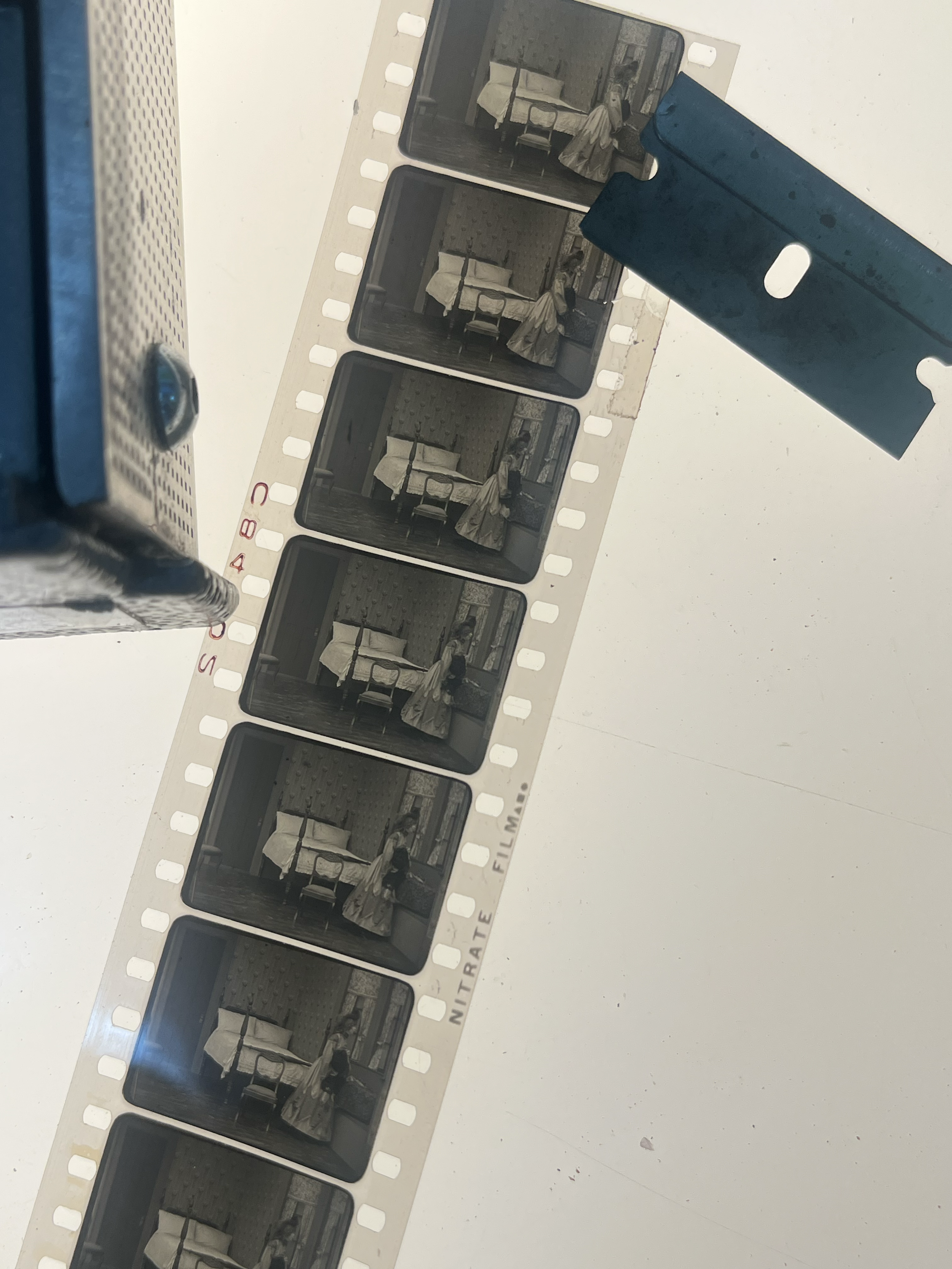 Six black-and-white nitrate negatives of a woman in a room, carrying a bag and wearing a dress and wide-brimmed hat, laid out on a white table with some equipment nearby.