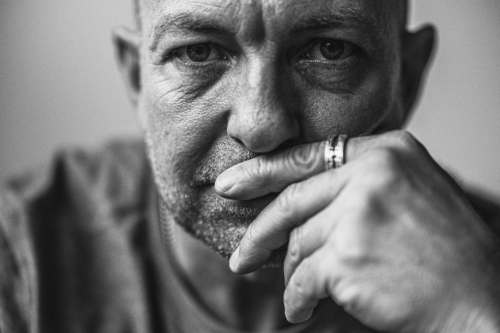 Close-up black and white portrait of a man with a contemplative expression, resting his hand against his face.