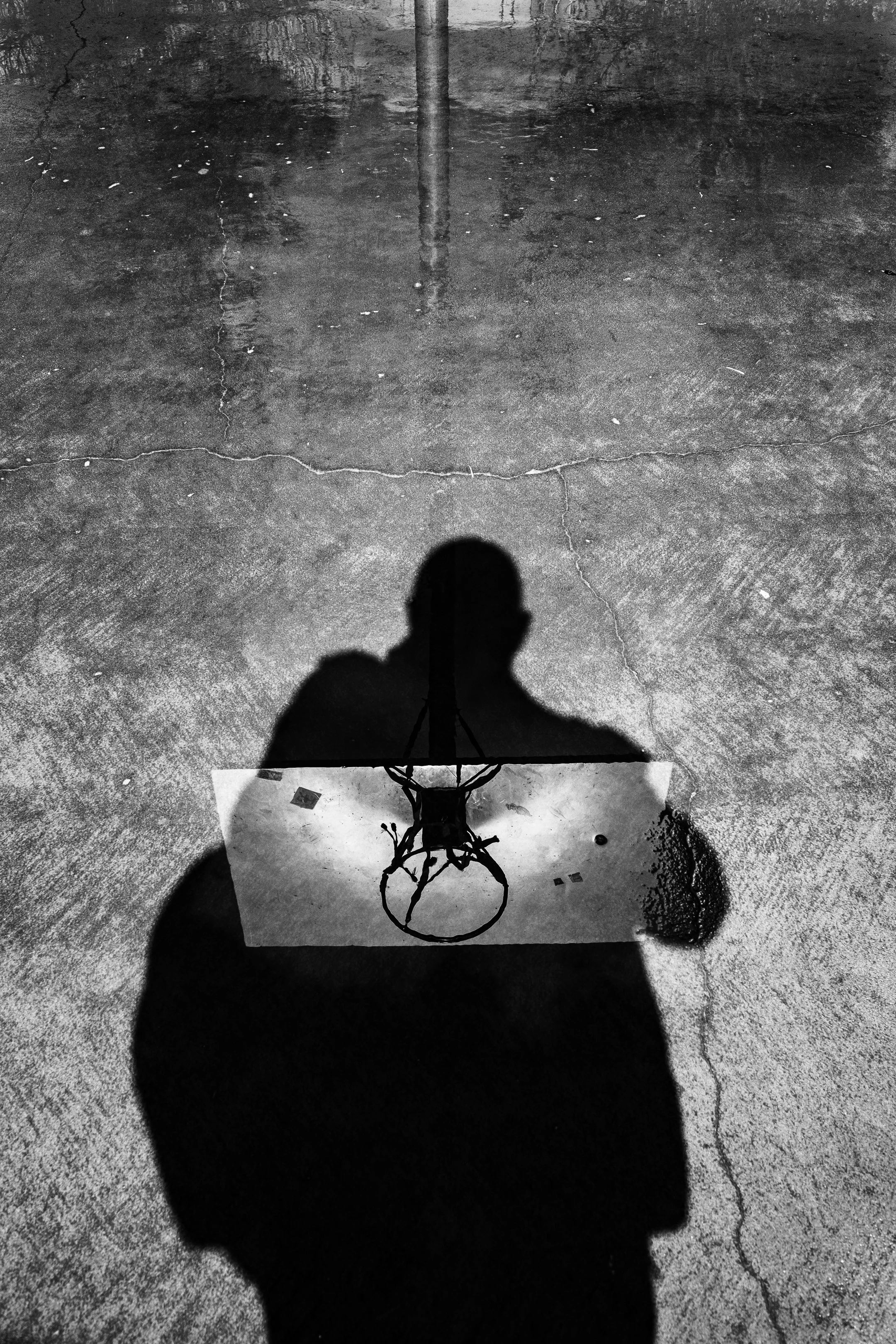 Shadow of a person holding a ring-like object on a wet, textured concrete surface with cracks.
