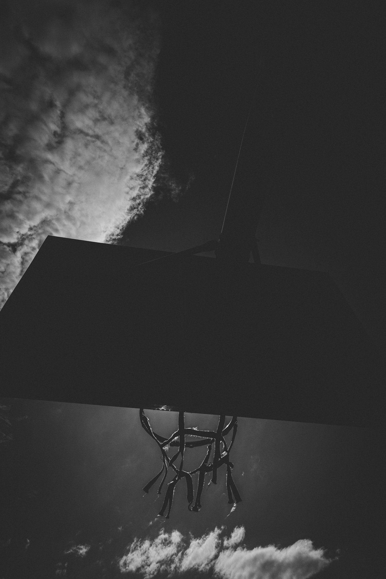 A basketball hoop photographed from below against a cloudy sky, with sunlight shining through the clouds.