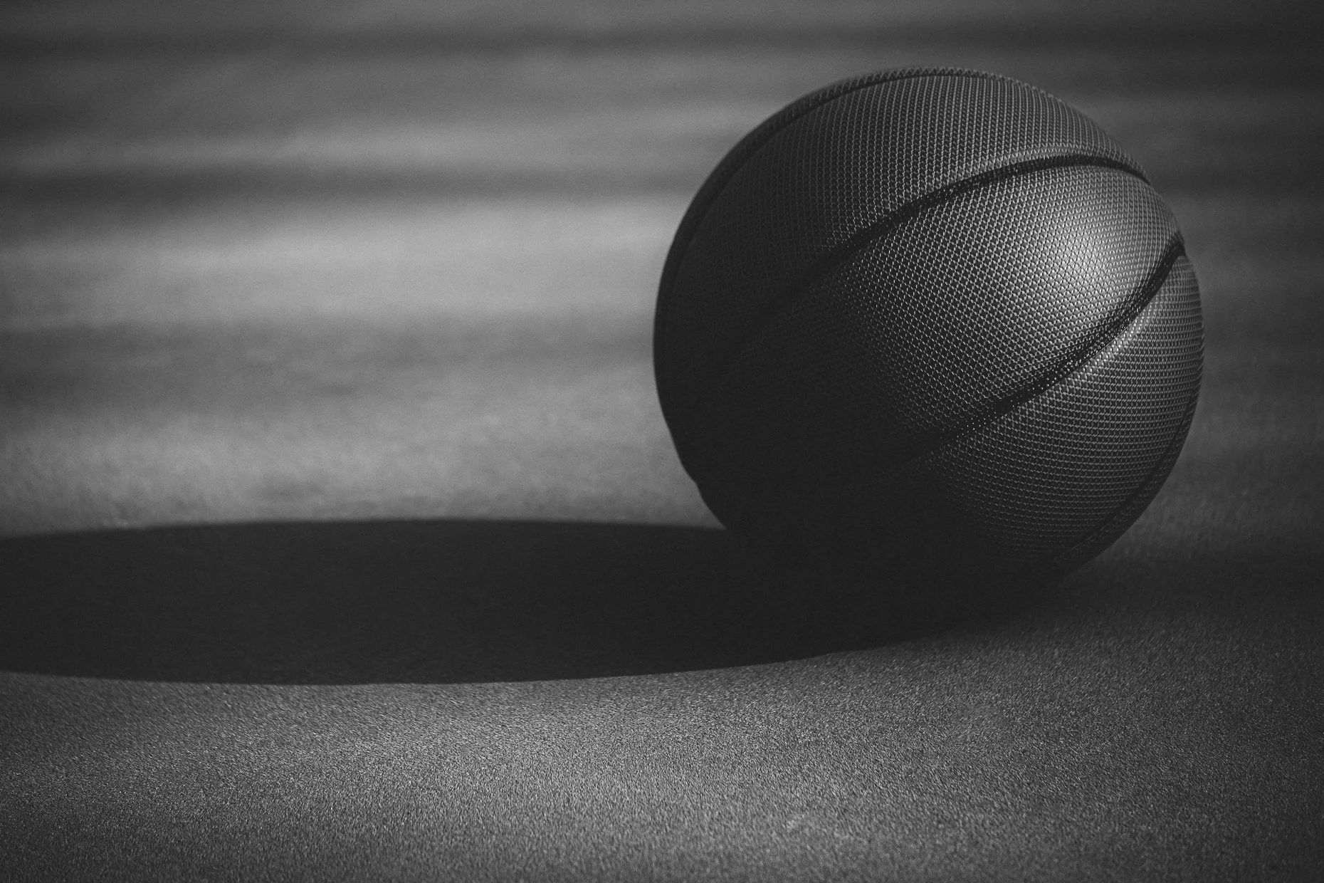 A black textured basketball resting on a smooth surface with a shadow cast to the left.