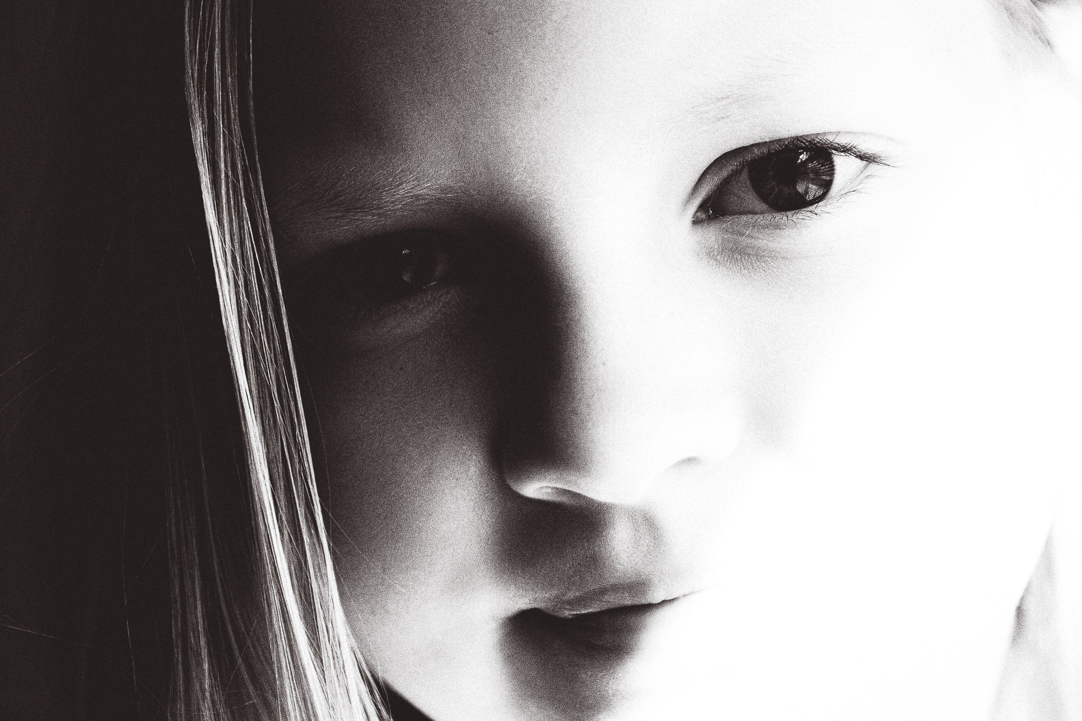 Close-up black-and-white photograph of a young girl's face, showing her eyes, nose, and lips with soft lighting.