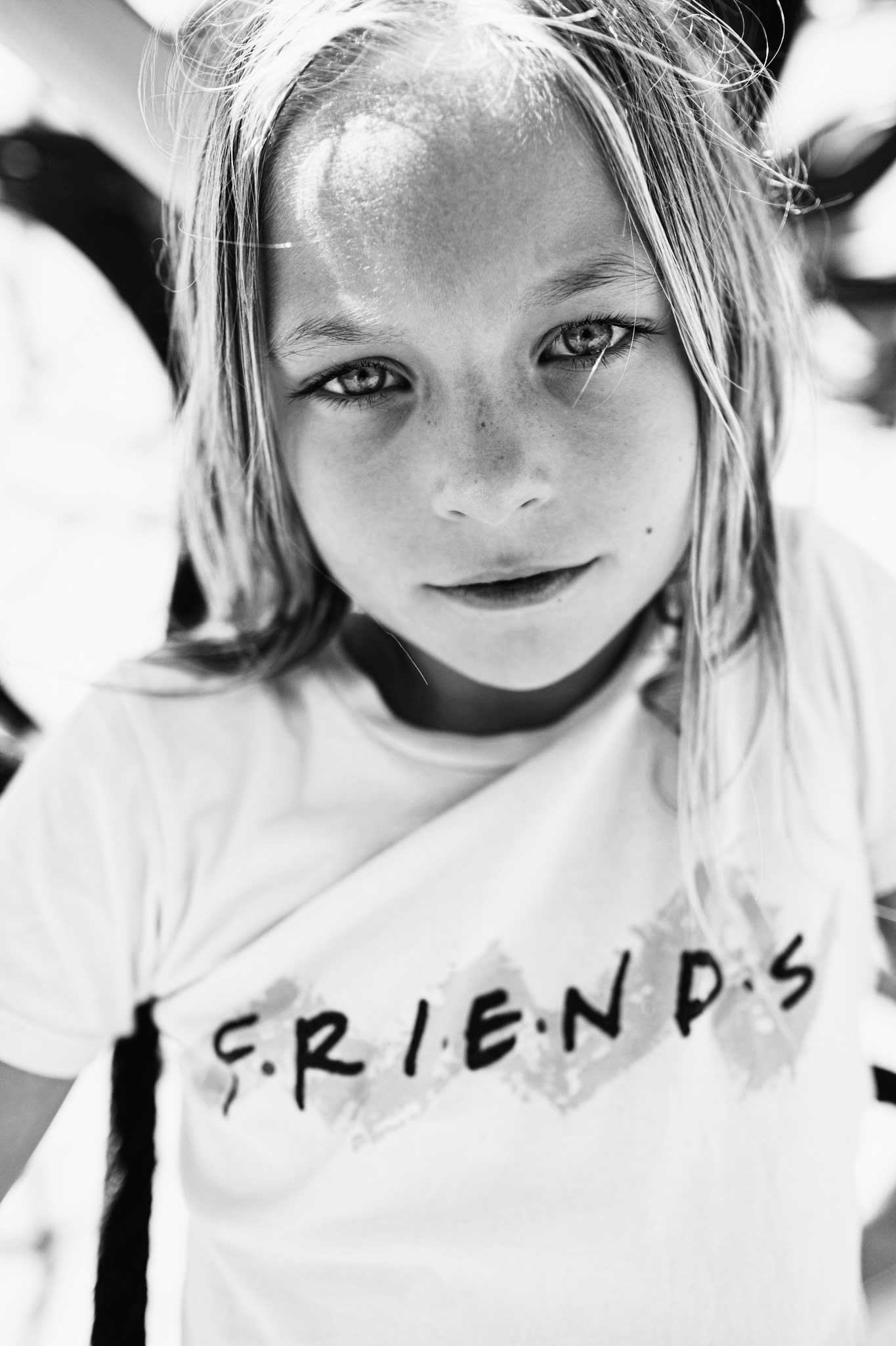 A young girl with wet hair, freckles, and light-colored eyes wearing a T-shirt with the word 'FRIENDS' on it, looking up at the camera.