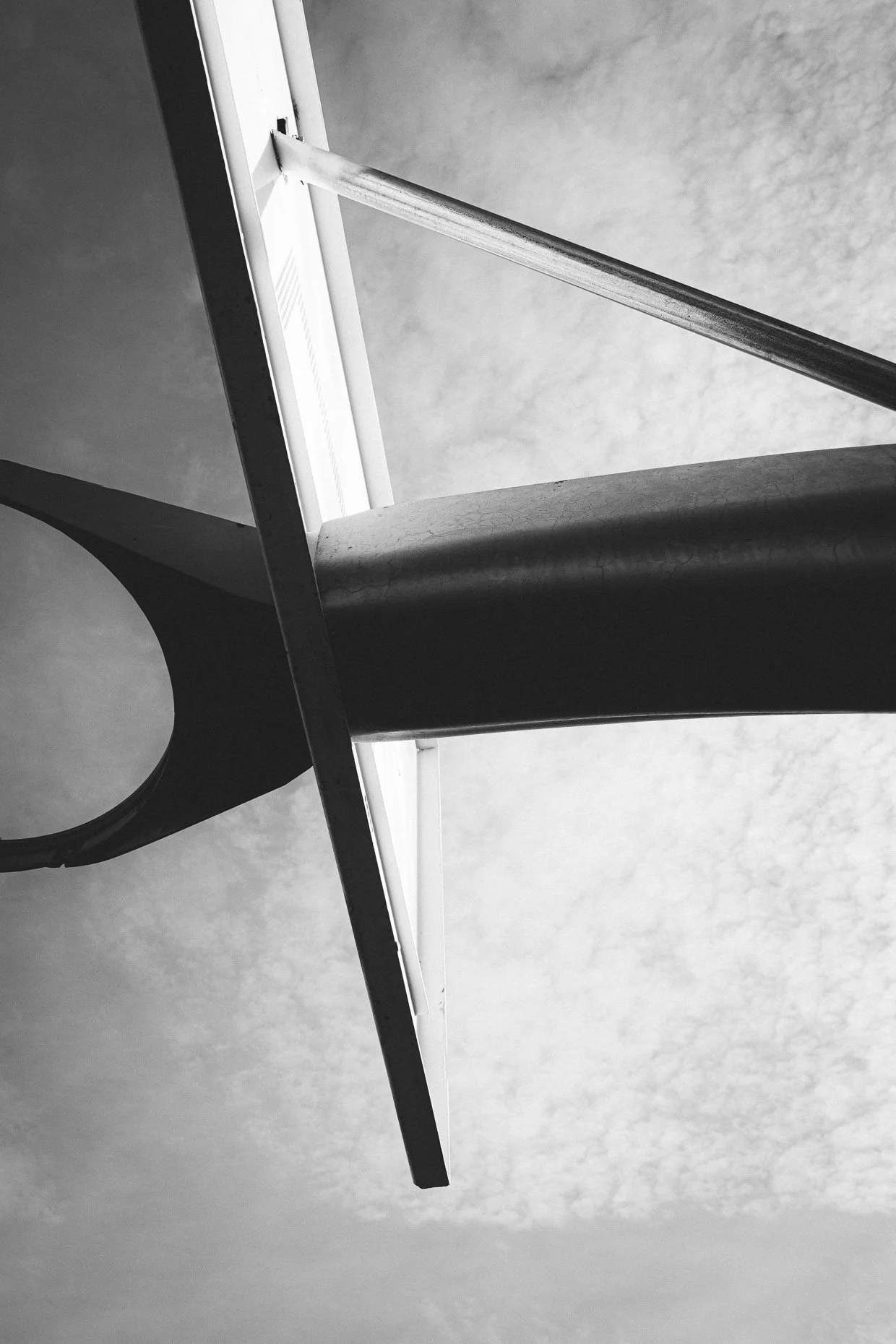Black and white photograph of a basketball hoop and backboard, viewed from below, against a cloudy sky.