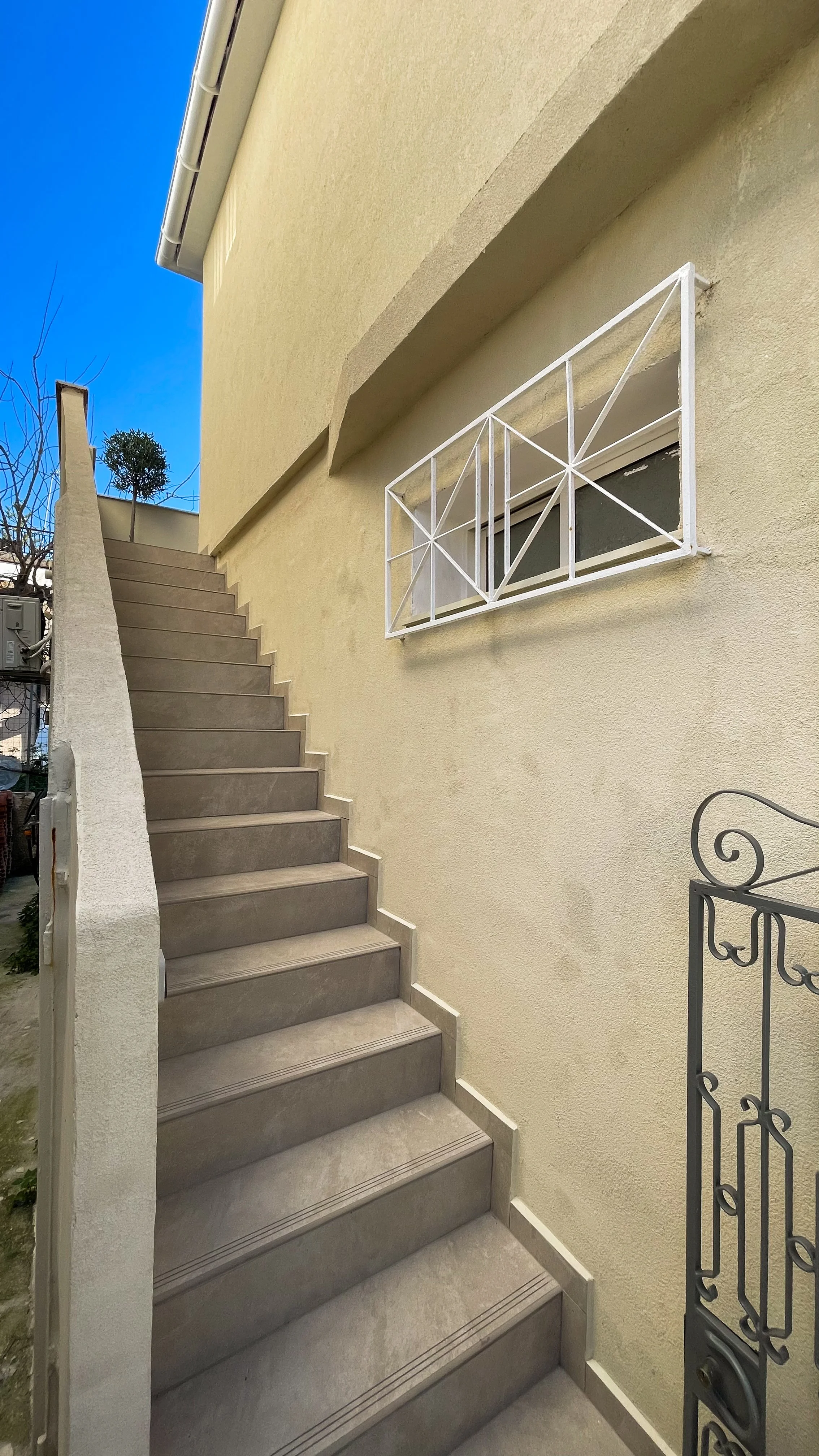Outdoor staircase attached to a beige building with a white railing and a small window on the wall.