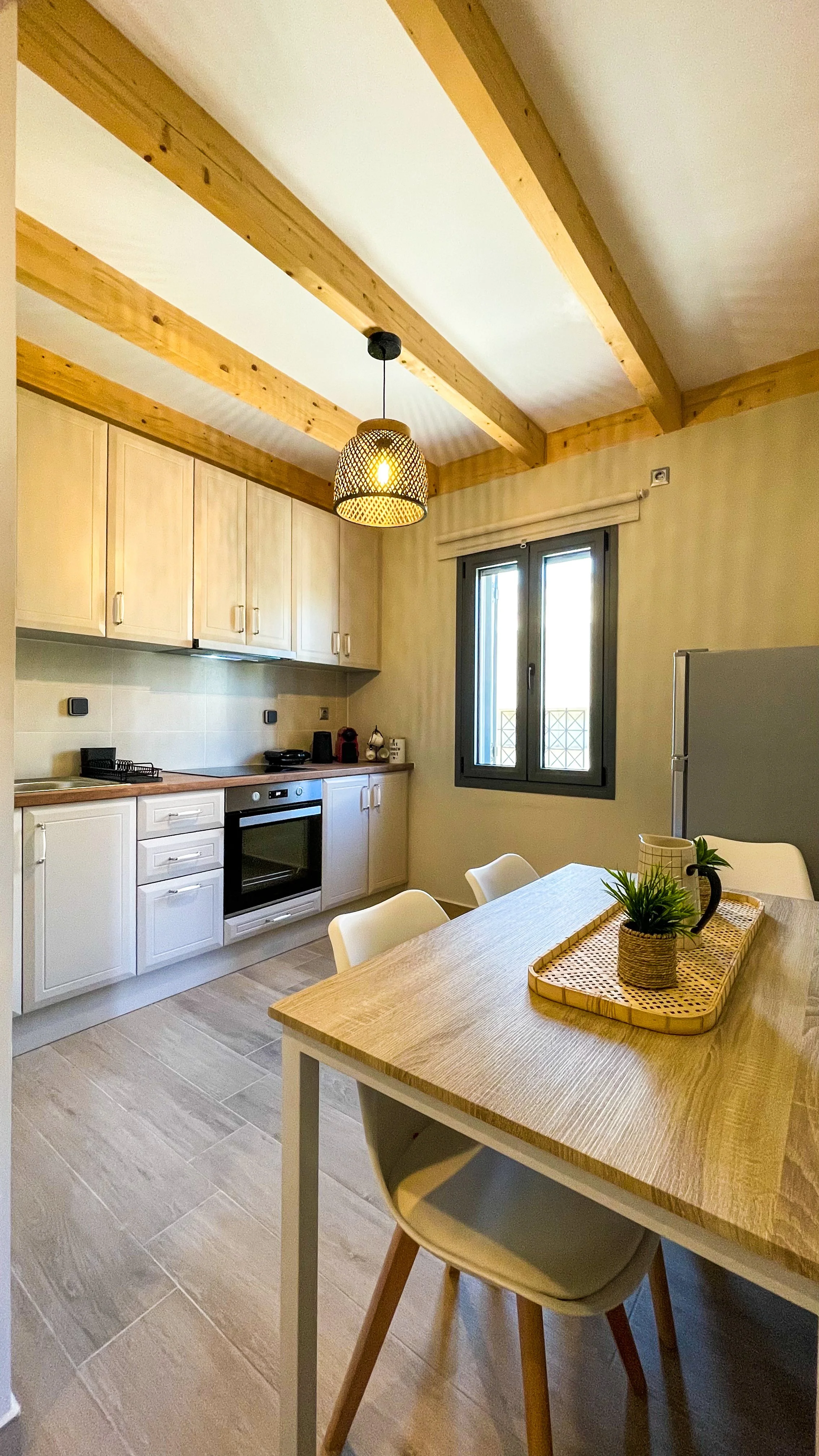 Modern kitchen with wooden beams, white cabinets, a stove, and dining table with chairs. A pendant light hangs from the ceiling.