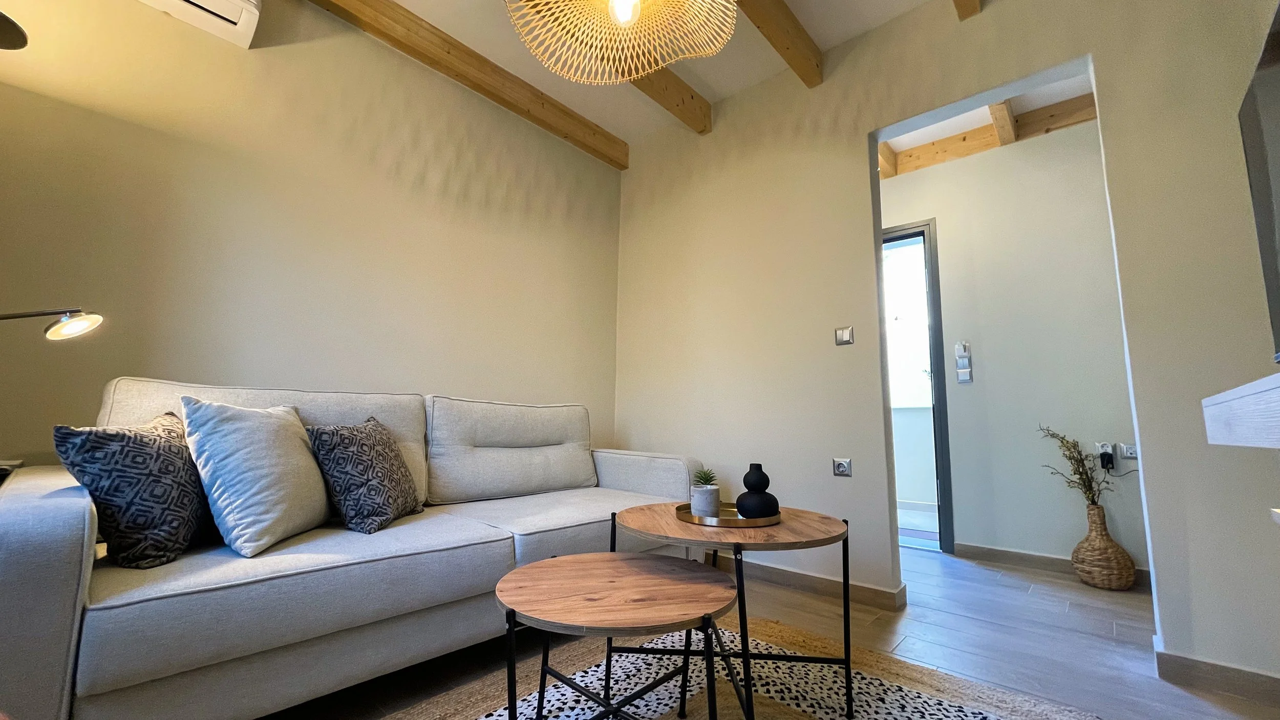 Modern living room with a beige sofa, decorative pillows, round wooden coffee tables, and a woven ceiling light fixture.
