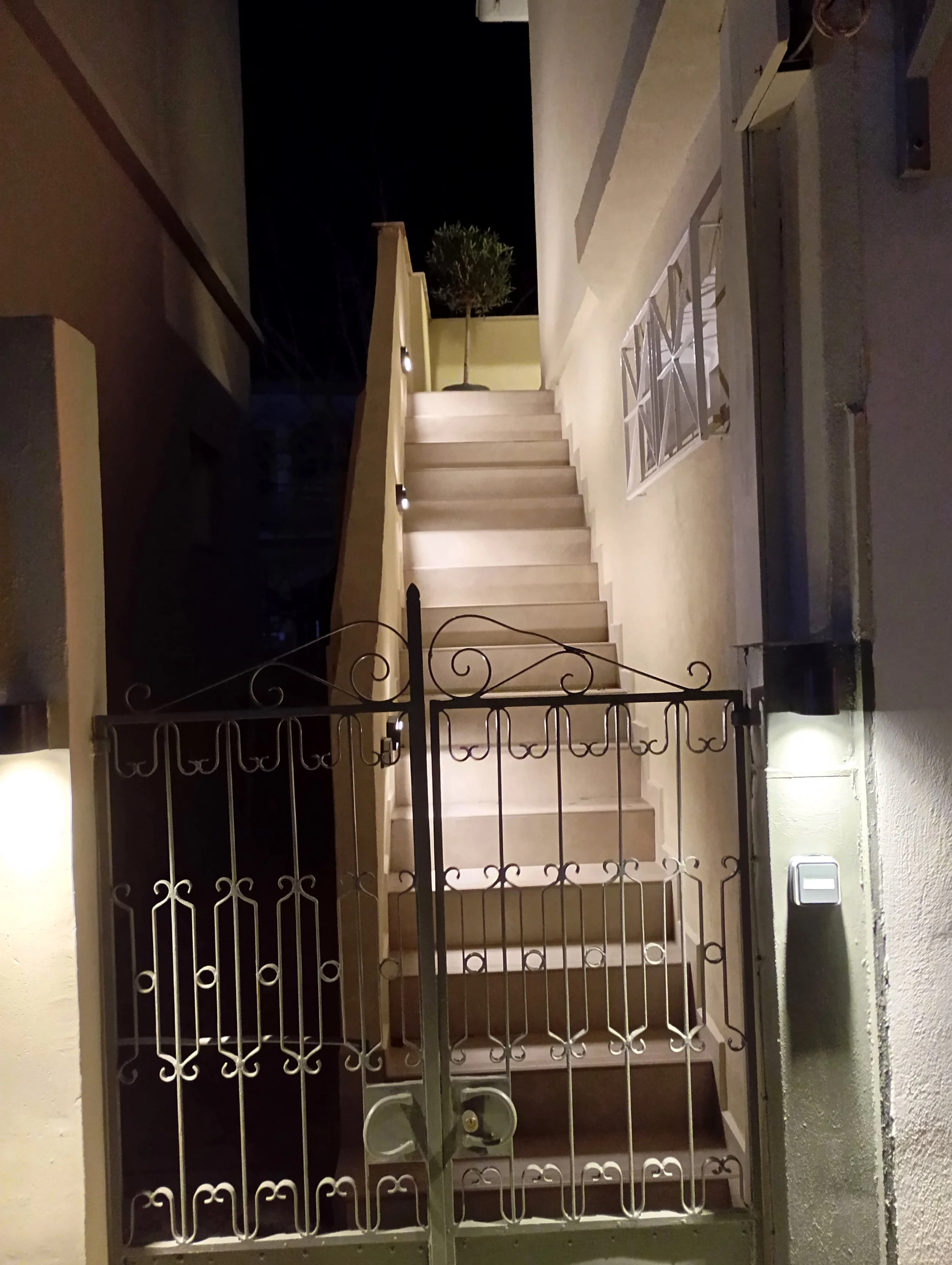 Outdoor staircase with metal gate at night, illuminated by wall lights.