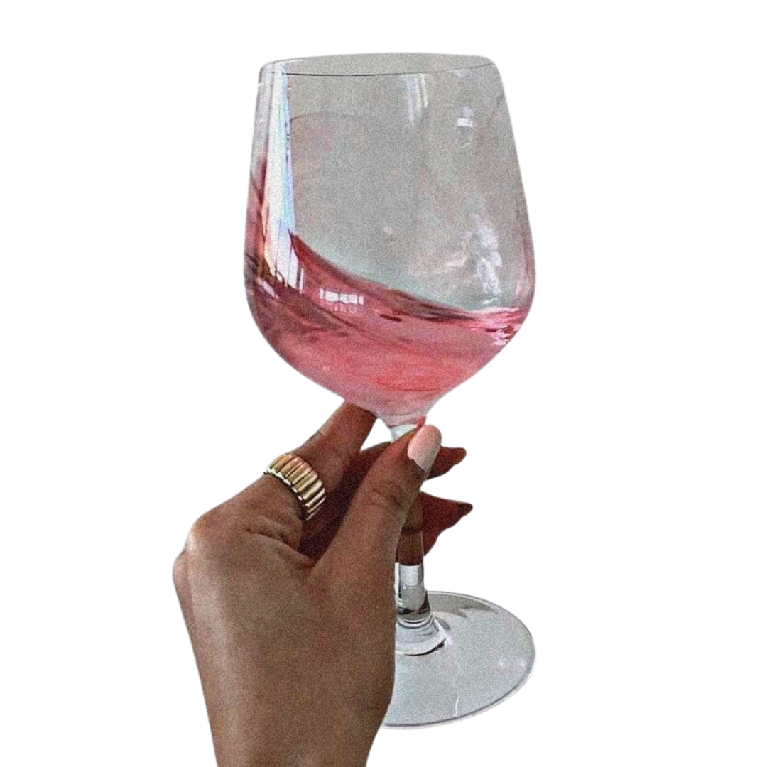 A hand holding a wine glass filled with pink wine or beverage against a black background.