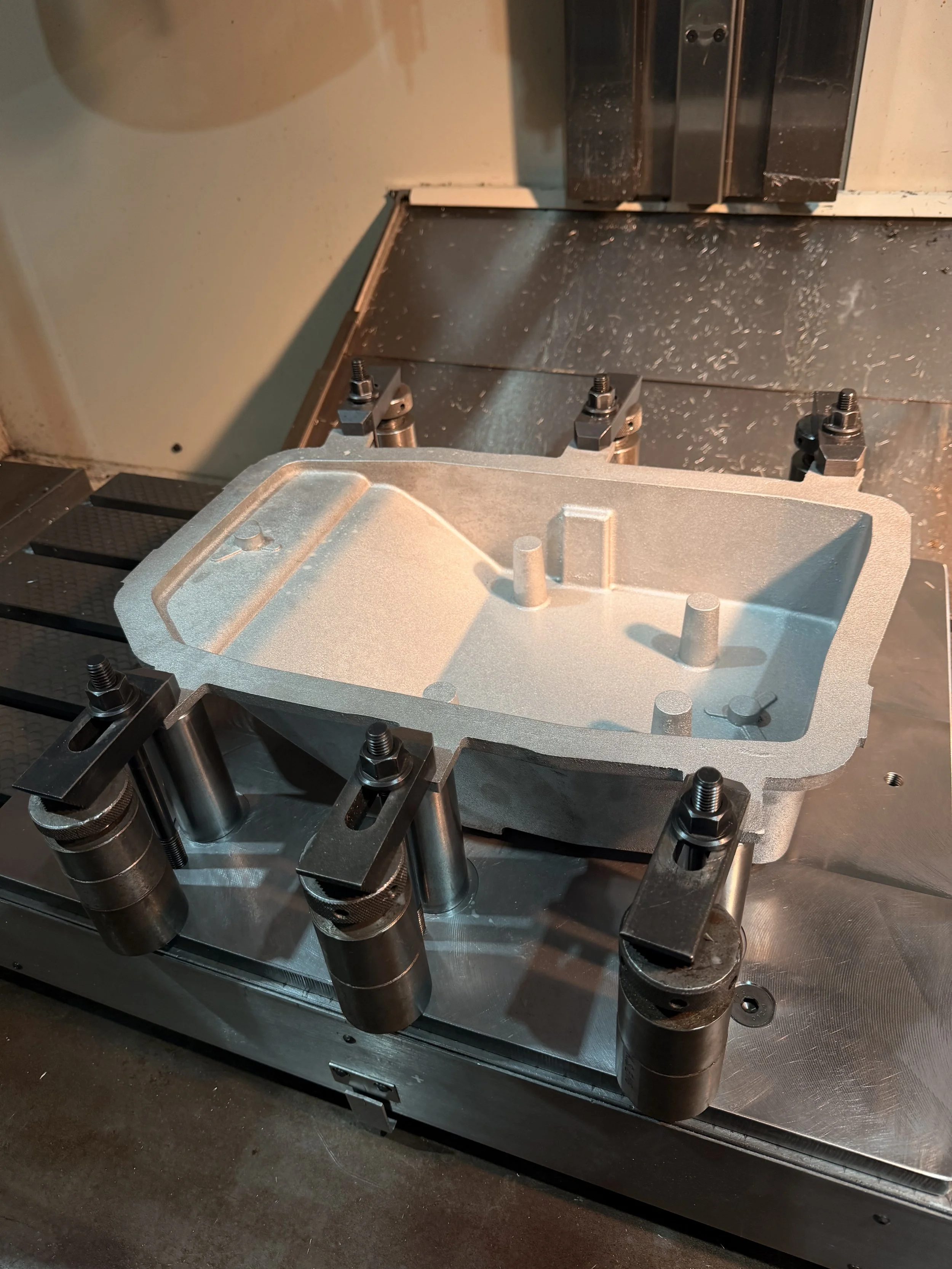 Close-up of a CNC machine with a metal workpiece clamped in a machining fixture, surrounded by metal shavings.