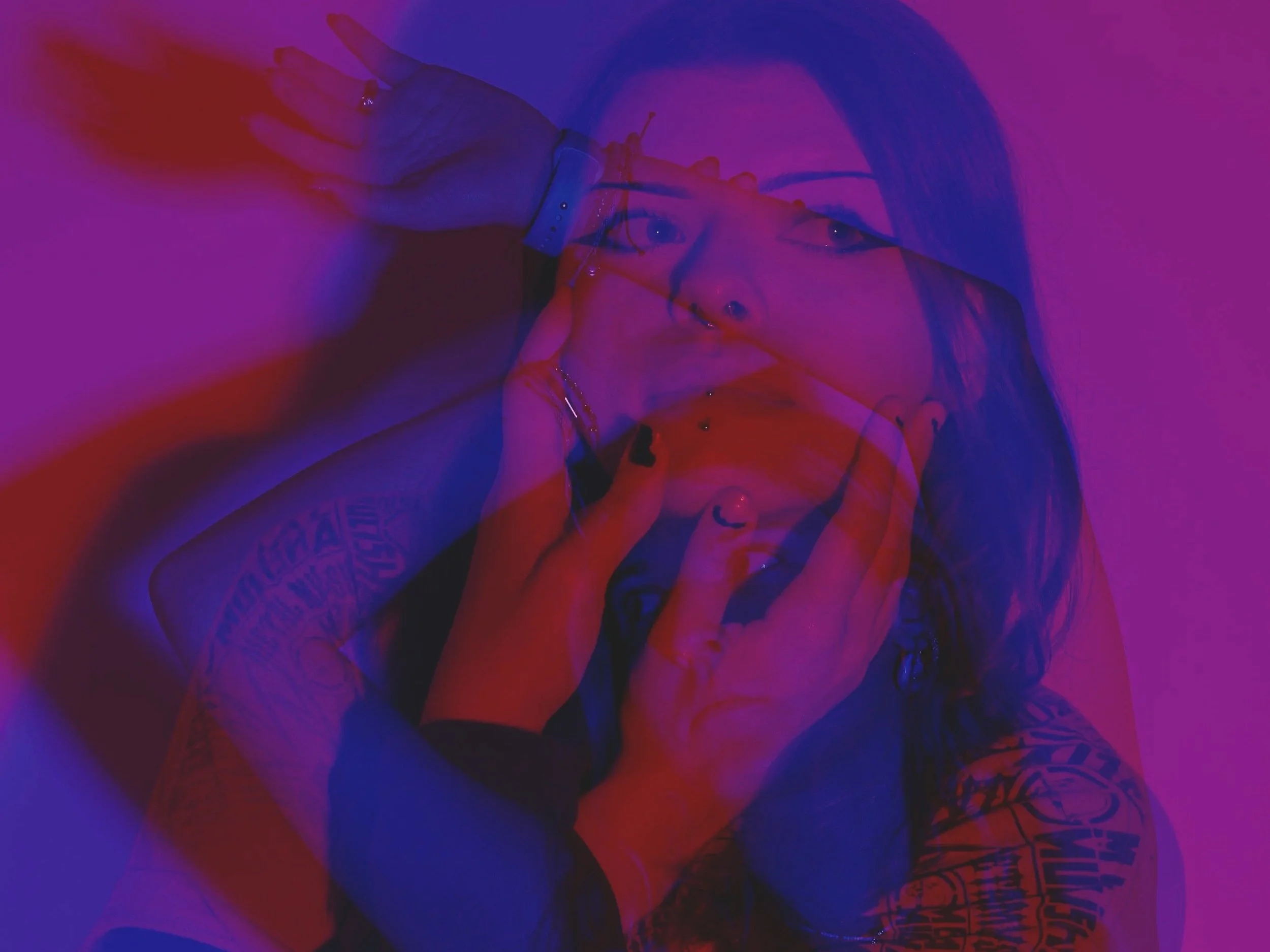 A layered, artistic photograph of two women with tattoos and jewelry, holding their faces with their hands, under pink and purple lighting.