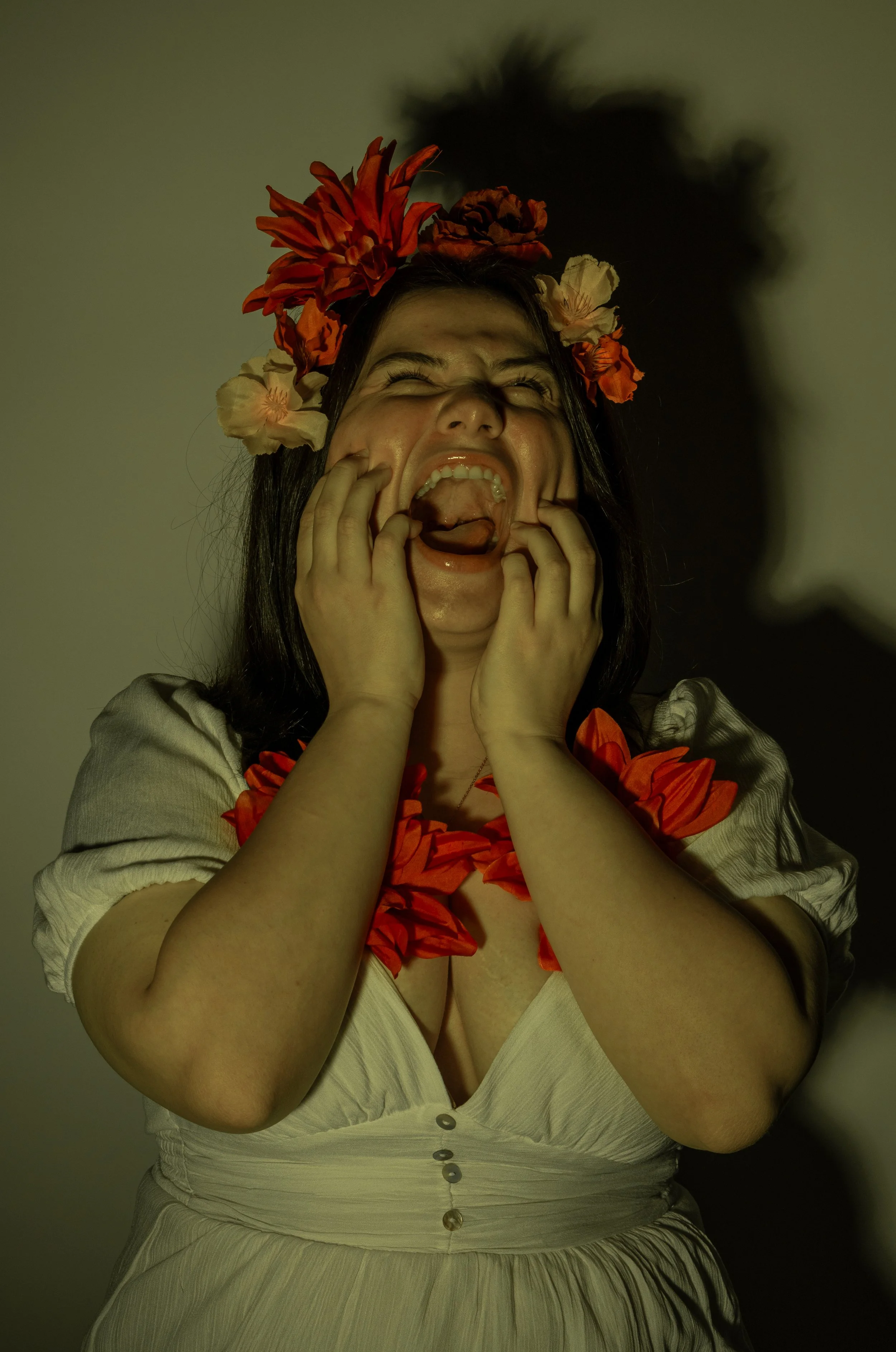 A woman with a flower crown and lei is making a dramatic, distressed facial expression, with her hands on her cheeks and her mouth open wide.