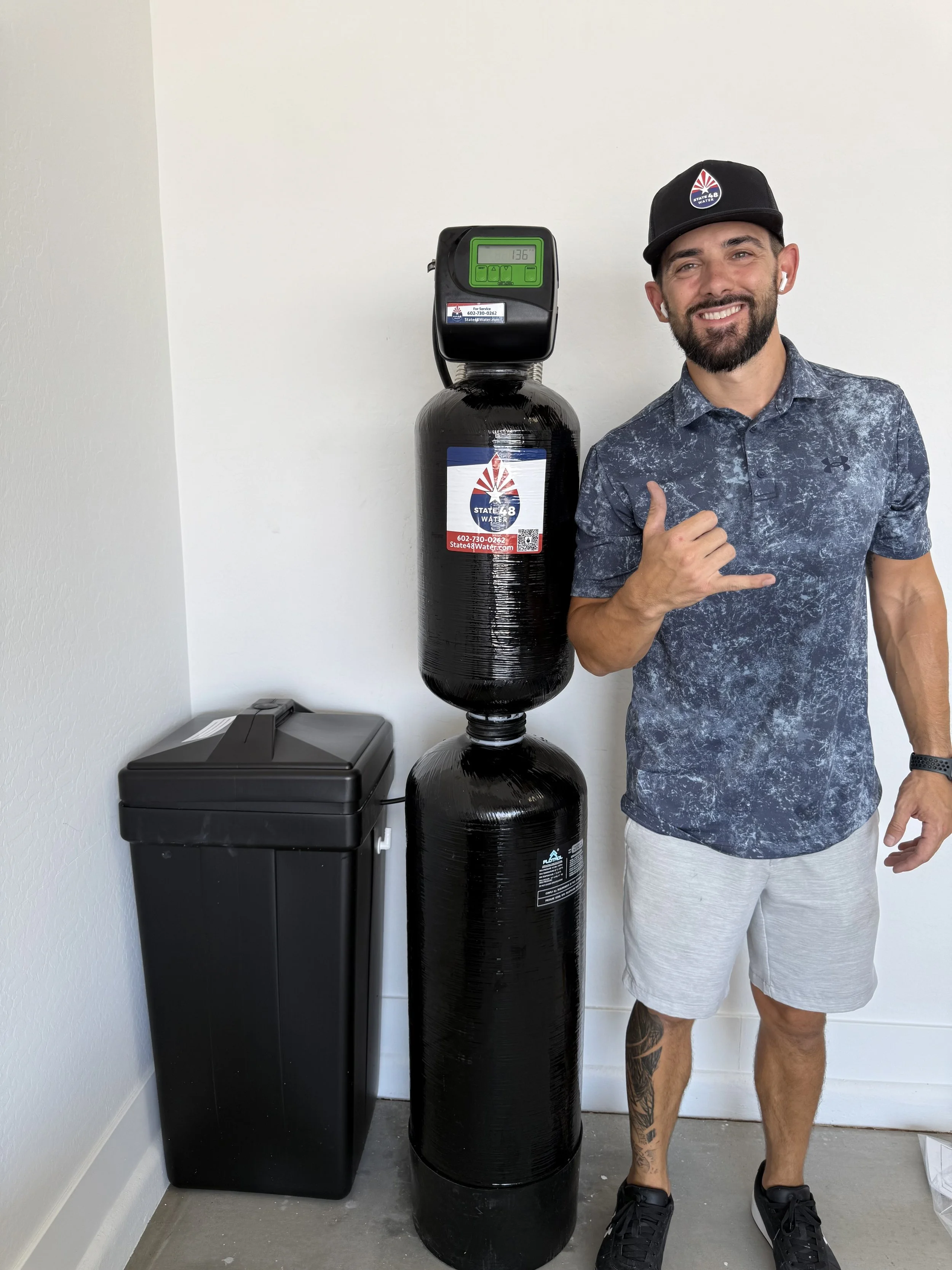 Man standing next to a newly installed whole house water treatment system with softener and filter, representing professional installation by State48Water.