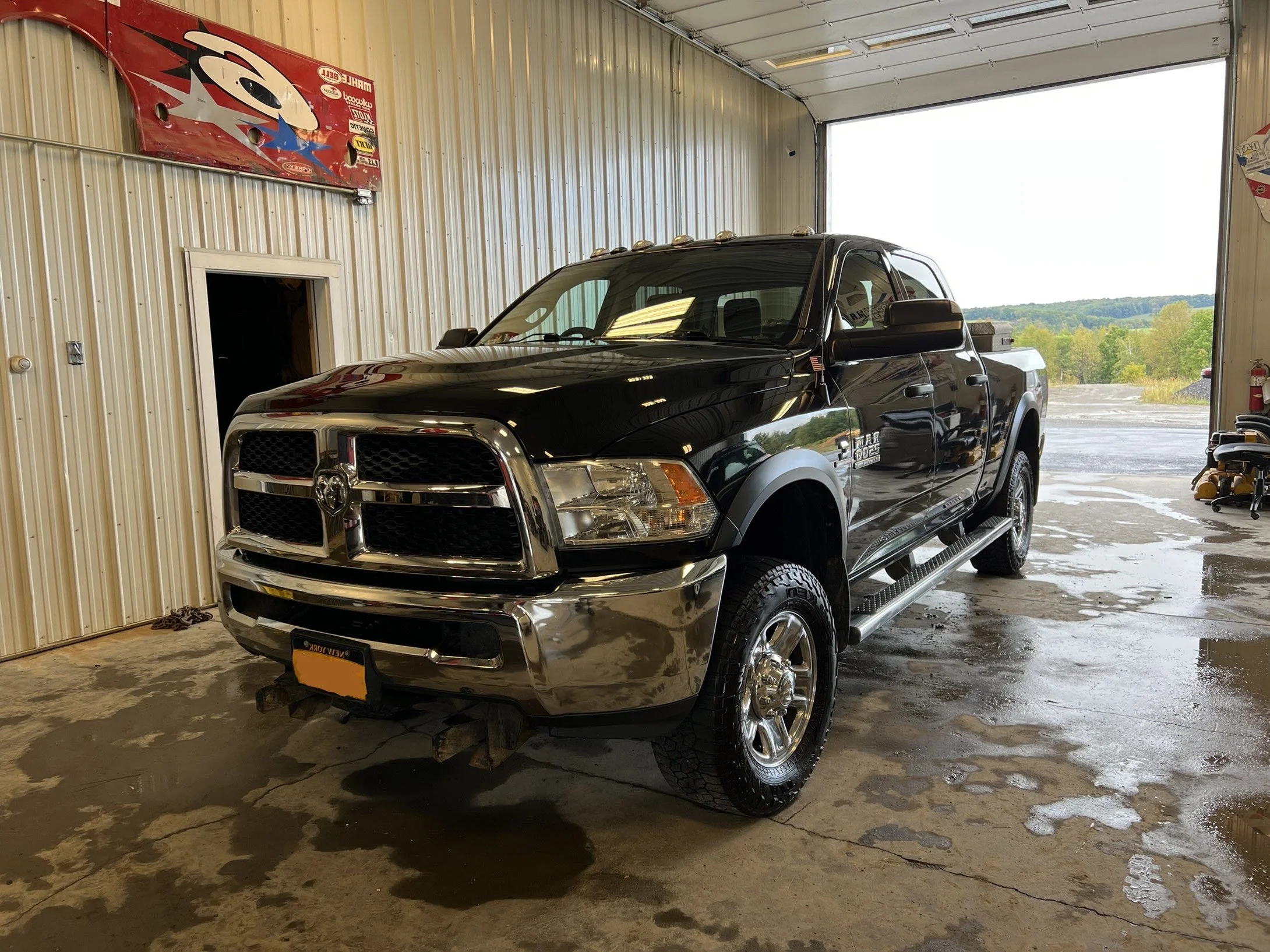 A black Ram pickup truck parked inside a garage with an open door, allowing a view of the outdoors.