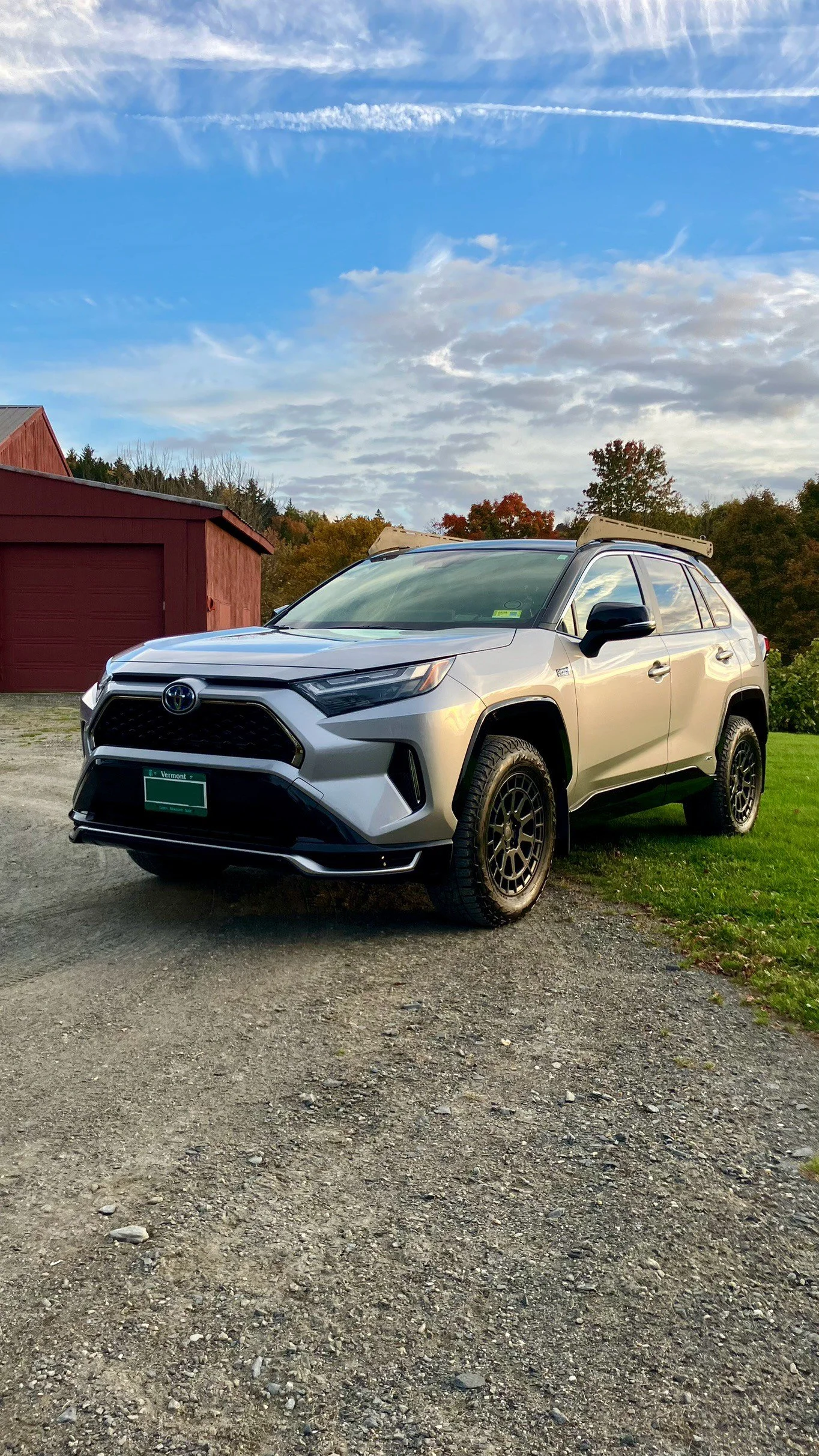 A silver Toyota SUV parked on a gravel path with a barn and trees in the background under a blue sky.