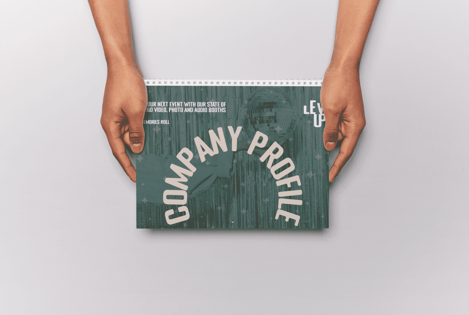 A flat lay mockup of the Level Up Booths digital Company Profile and event pricing brochure being held by two hands against a clean, minimal light grey background