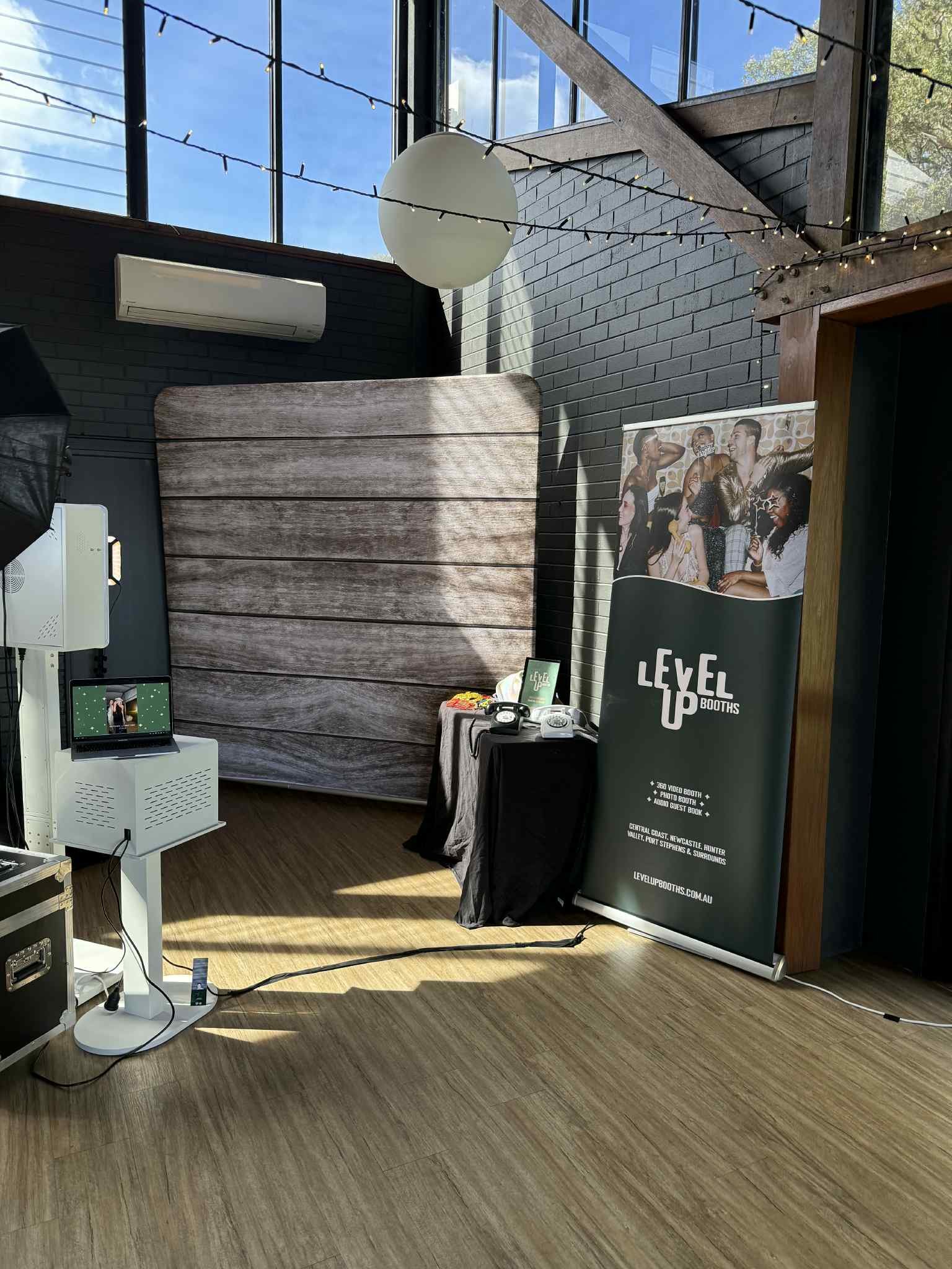 Modern open-air photo booth setup with a timber-look backdrop, audio guest book, and Level Up Booths branded banner for event hire in the Hunter Valley and Central Coast.