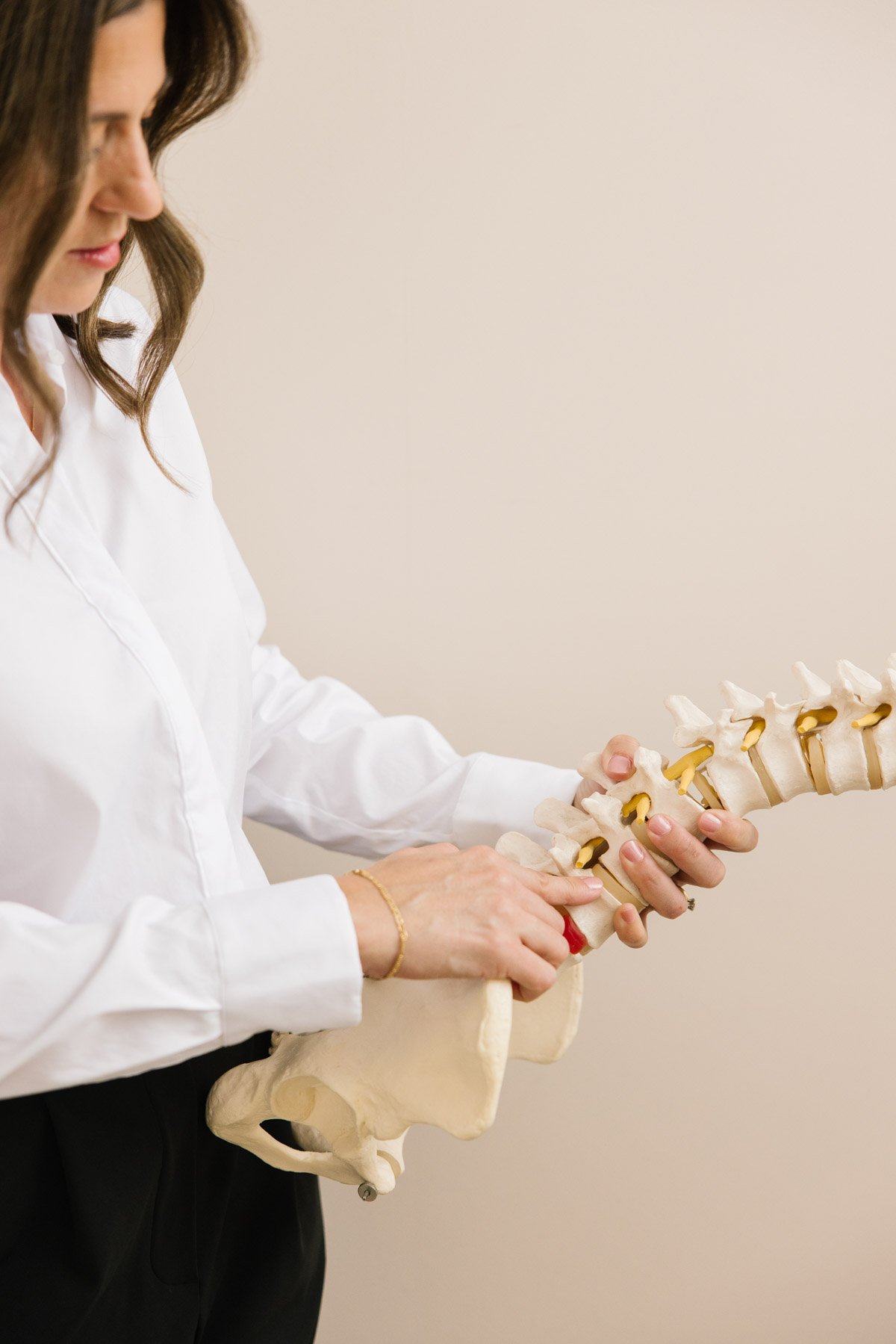 Stella from Stella Chiropractic holding a human spine model, wearing a white shirt, demonstrating anatomy.
