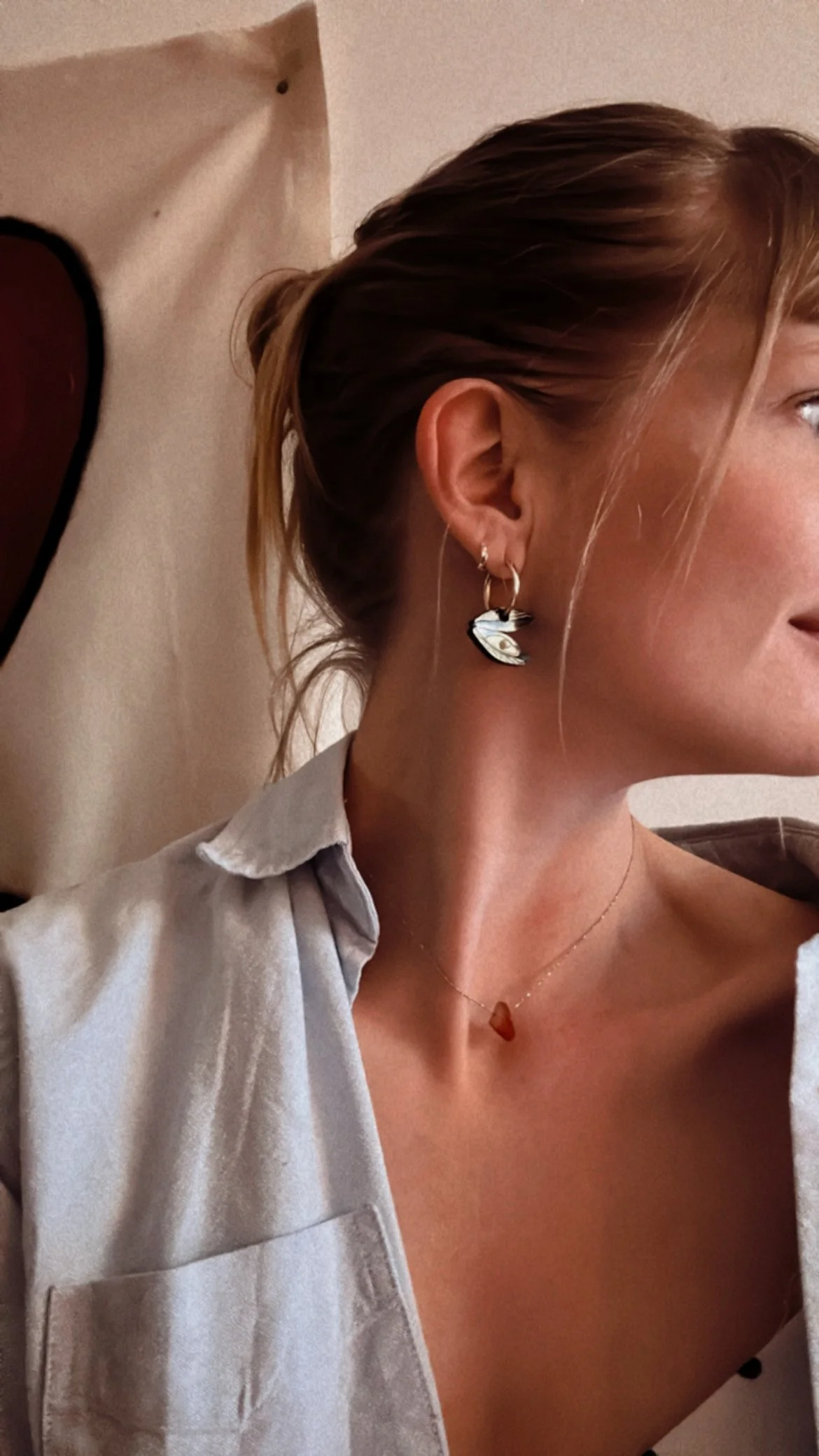 Femme portant une chemise, un collier et une boucle d'oreille, profil droit, fond blanc avec impression.