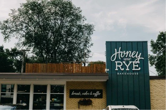 Exterior of Honey and Rye Bakehouse with signage and parked cars