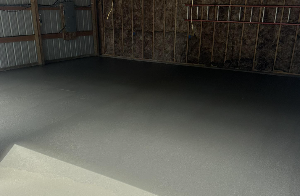 Unfinished garage with newly painted concrete floor, exposed wall insulation, and framing.