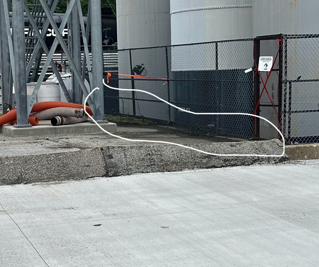 A construction site with orange and gray hoses, metal framework, a concrete curb, and a chain-link fence surrounding the area.