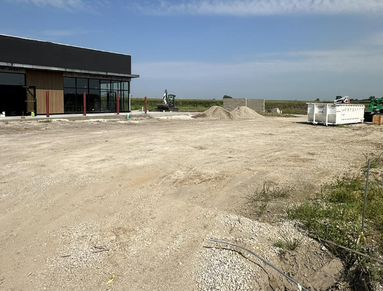 Construction site with a partially built structure, dirt ground, construction materials, and equipment under a clear sky.