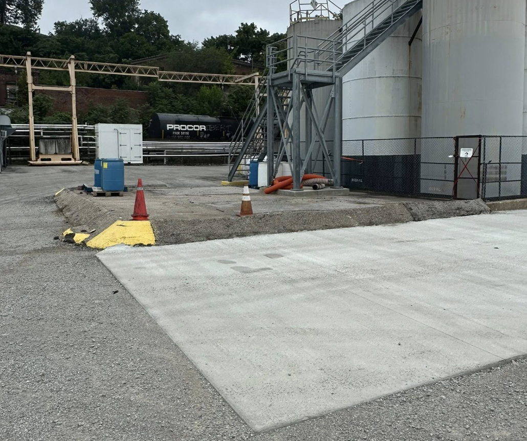 Construction site with a ramp, traffic cones, and safety barriers around a large storage tank.