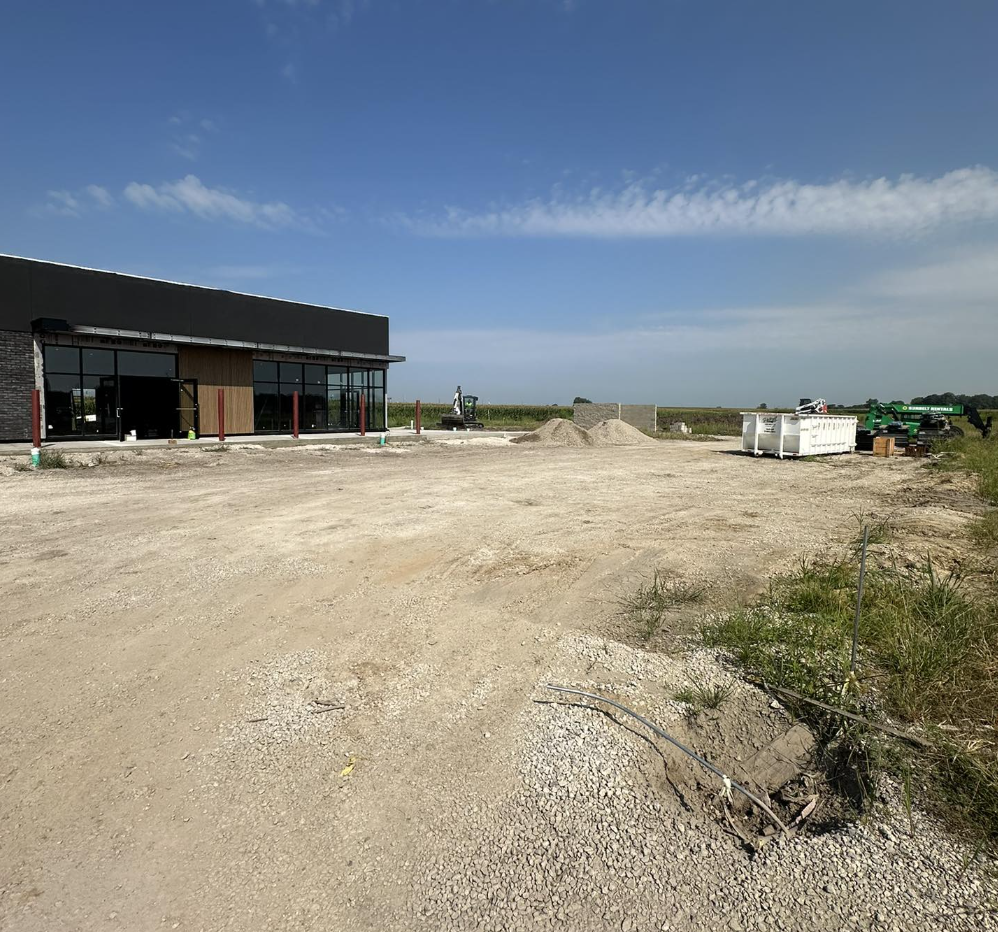 Construction site with a partially built commercial building, construction materials, and equipment under a blue sky with clouds.