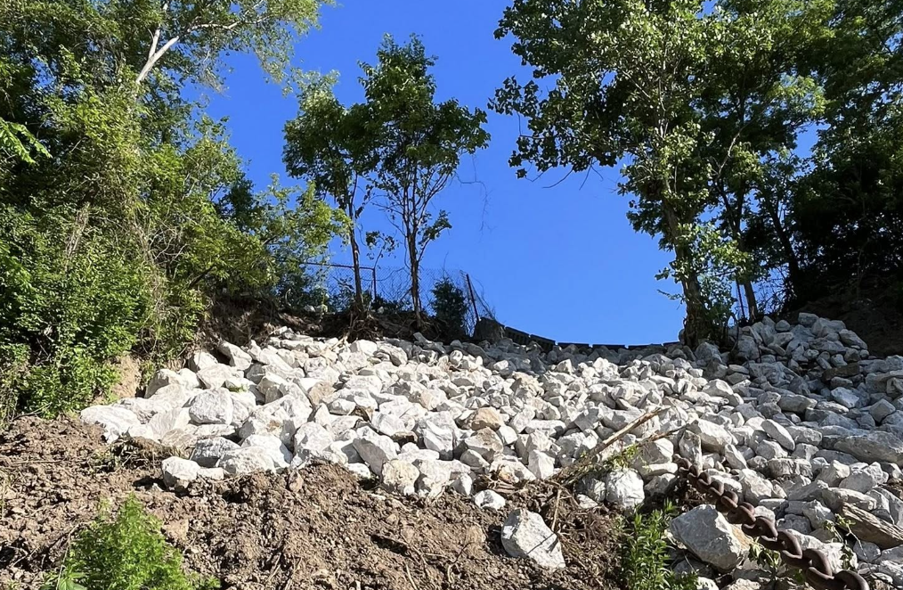 Rock debris and chain on a hillside with trees and blue sky in the background.