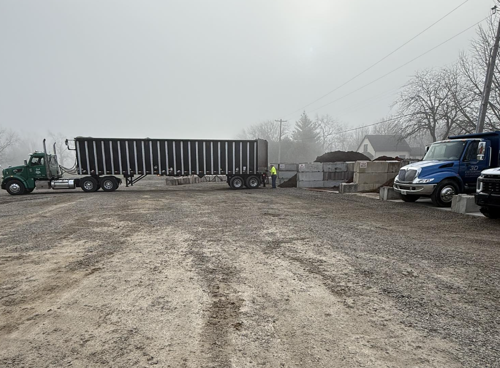 Construction site with large dump truck, concrete blocks, and a worker in a yellow safety vest on a foggy day.