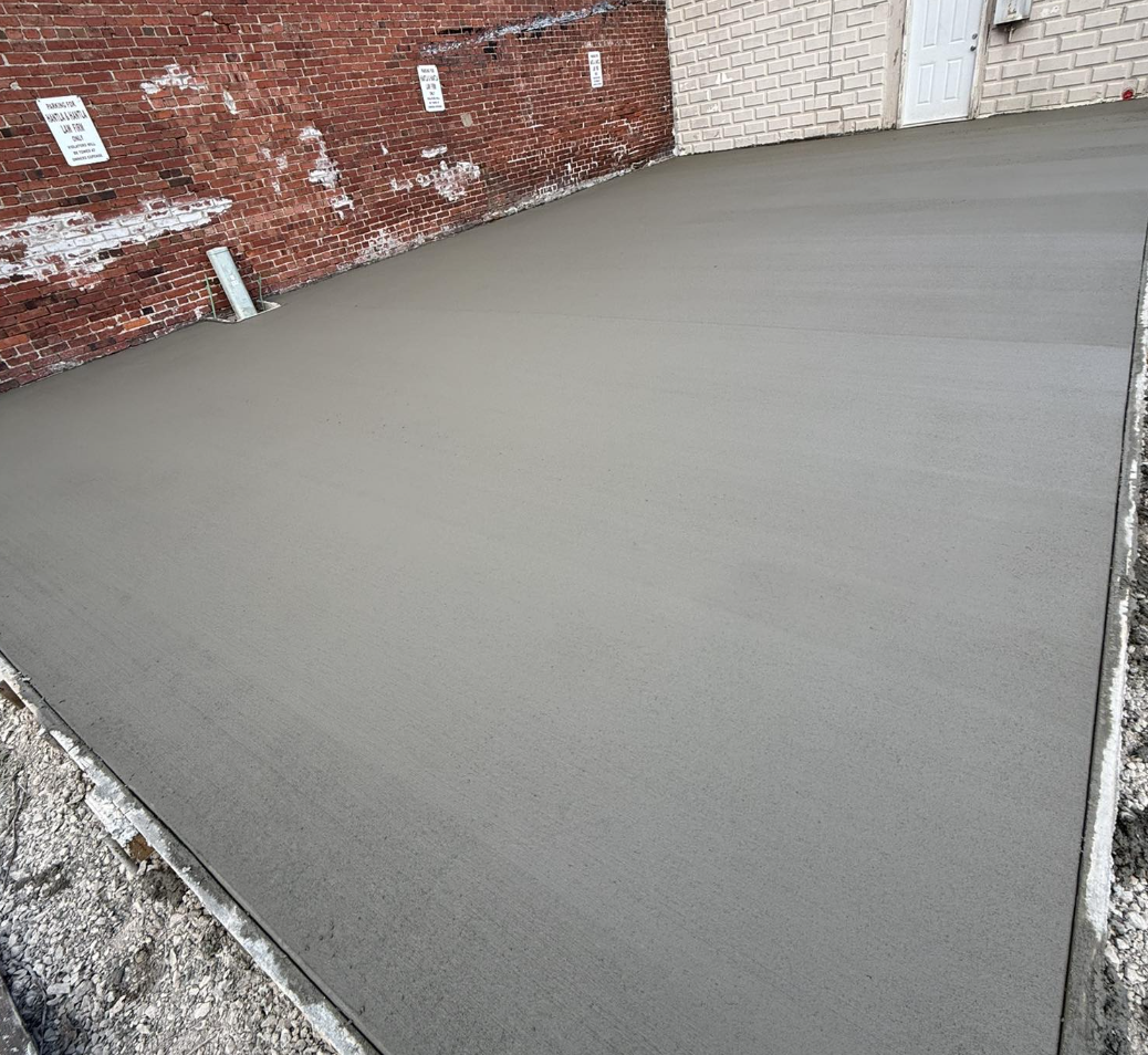 Freshly poured concrete slab on a building site, surrounded by gravel and brick walls.