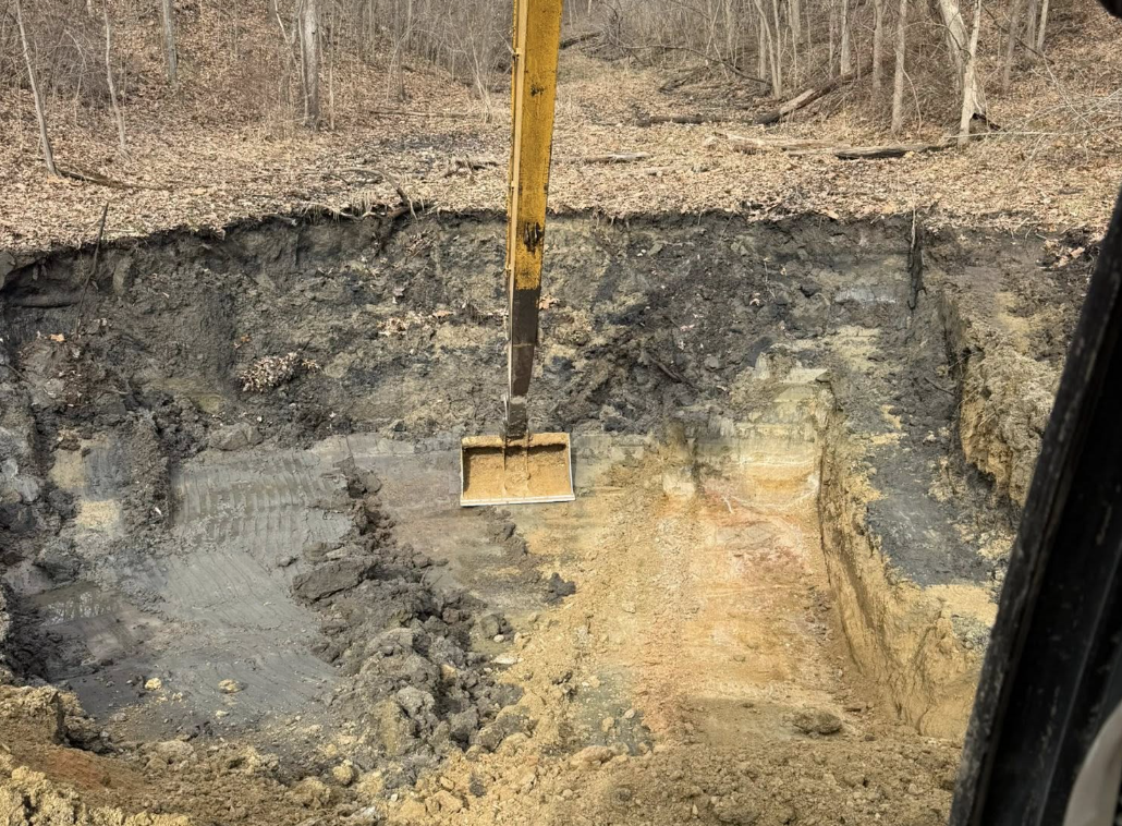 Construction excavation site with a yellow measuring stick, showing layers of soil and rock.