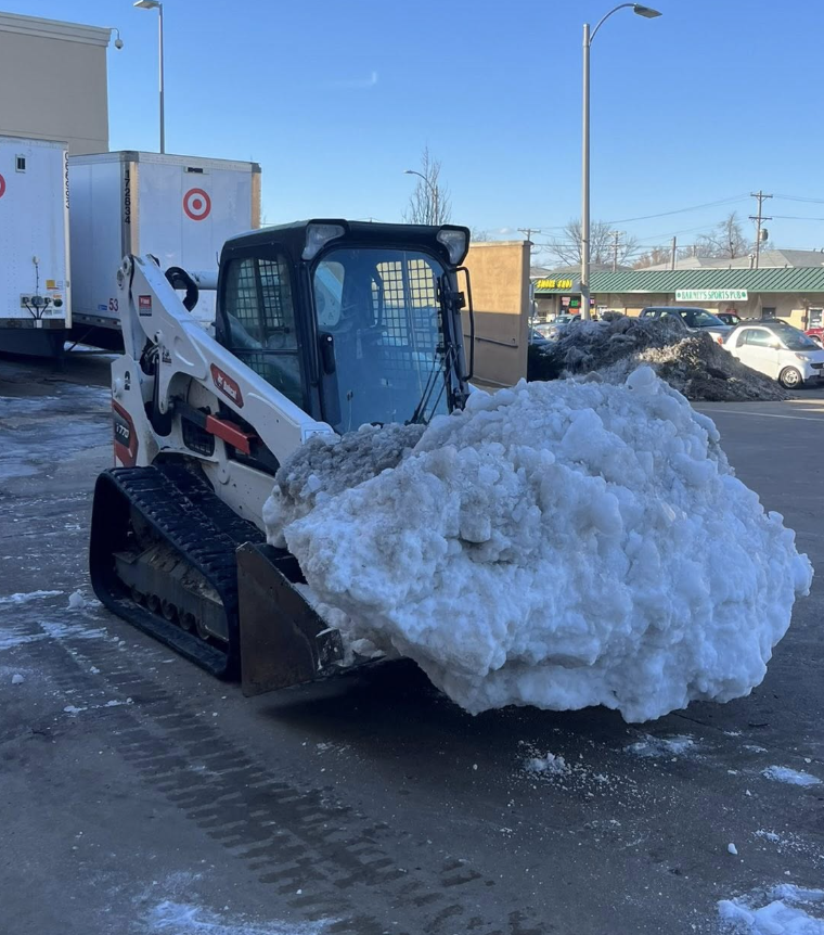A skid-steer loader clearing snow from a parking lot.