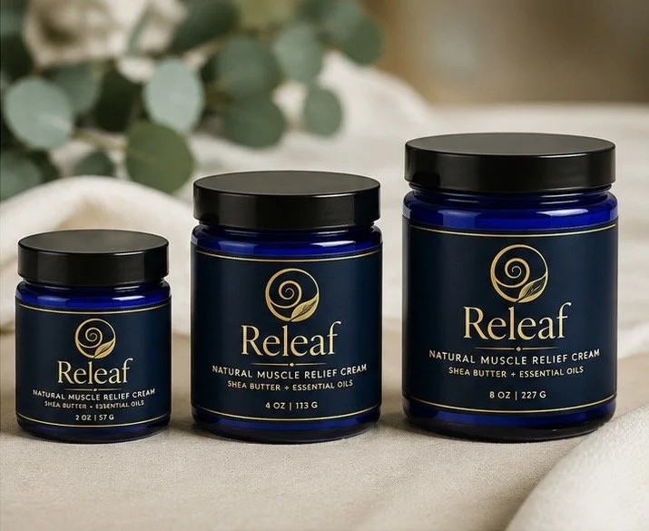 Three blue jars of Releaf natural muscle relief cream with shea butter and essential oils, arranged from small to large on a beige surface with green foliage in the background.